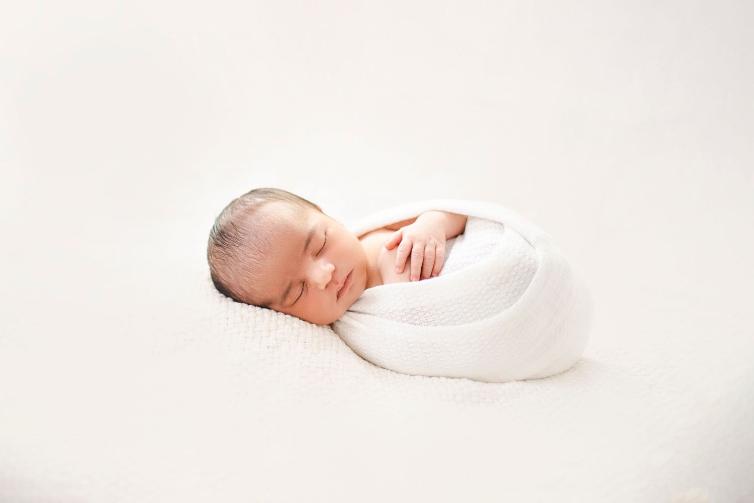 Sleeping newborn baby wrapped in white blanket on white background.