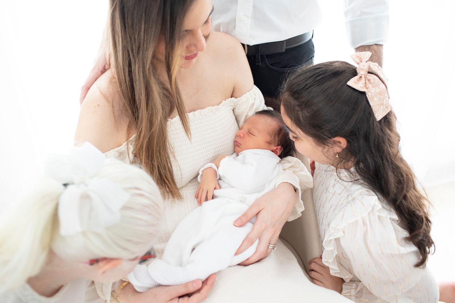 Intimate family portrait session with newborn baby in white against neutral background.