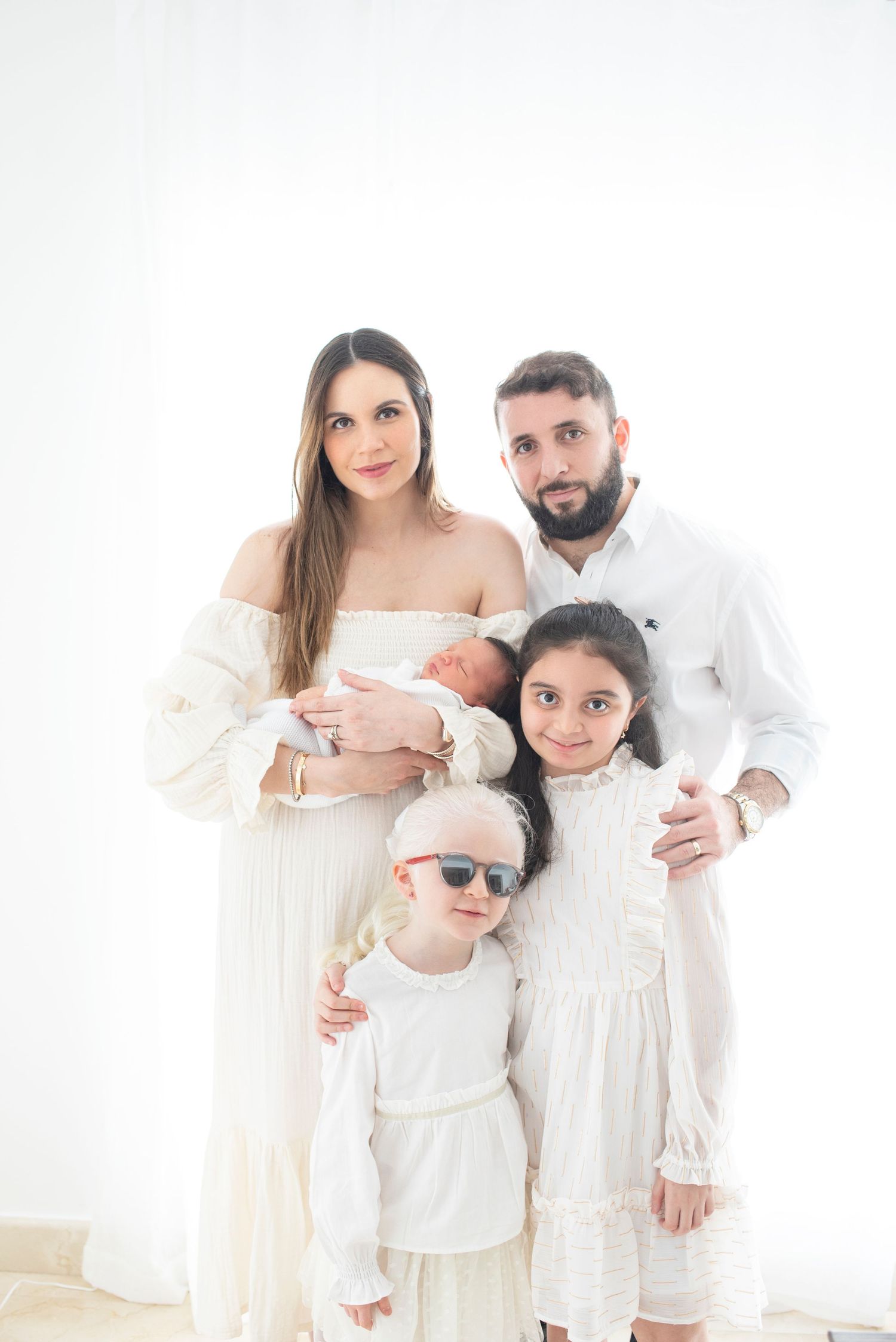 Family dressed in all white poses together for studio portrait session.