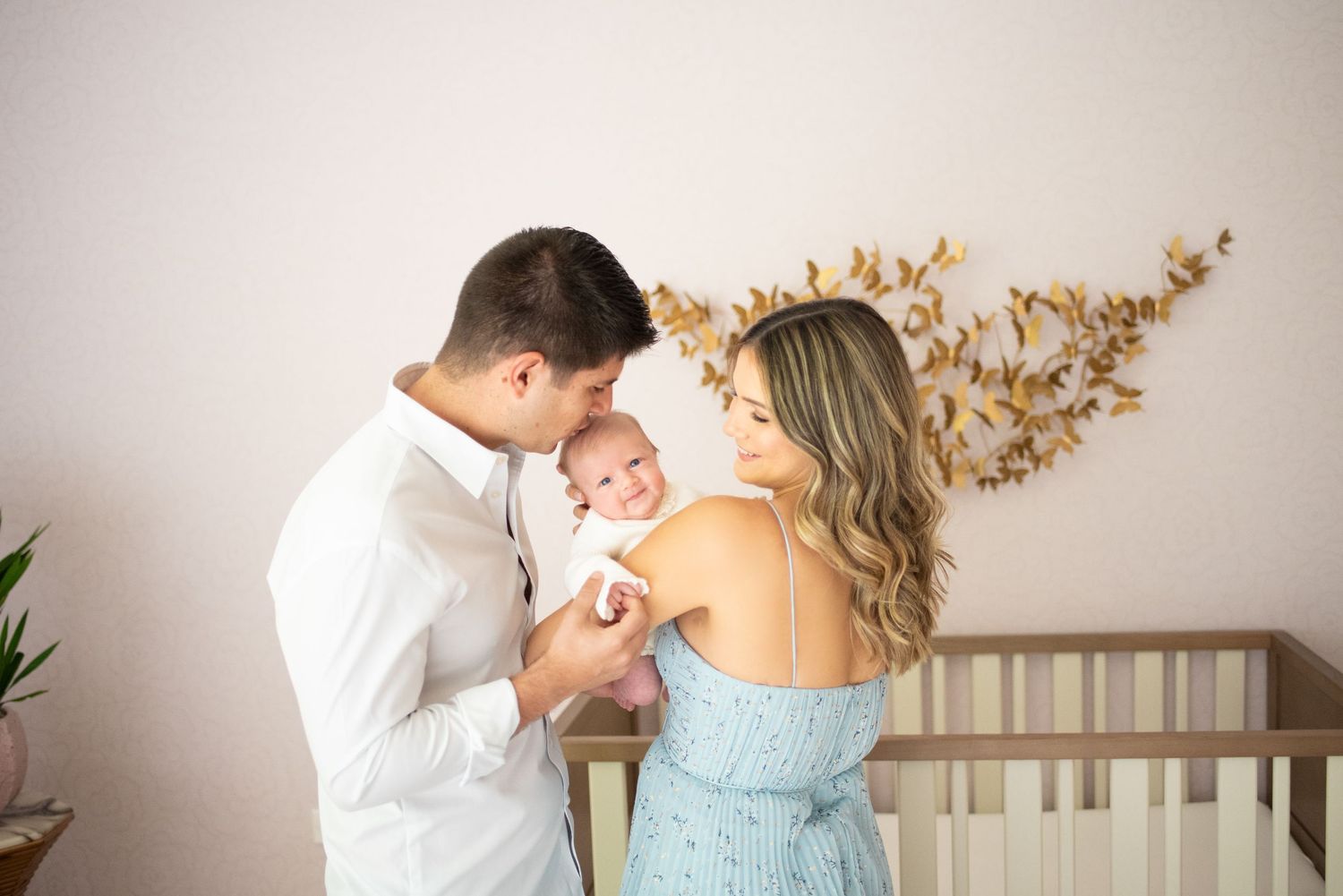 A romantic couple in formal attire embraces near a wall with golden floral decor in soft lighting.