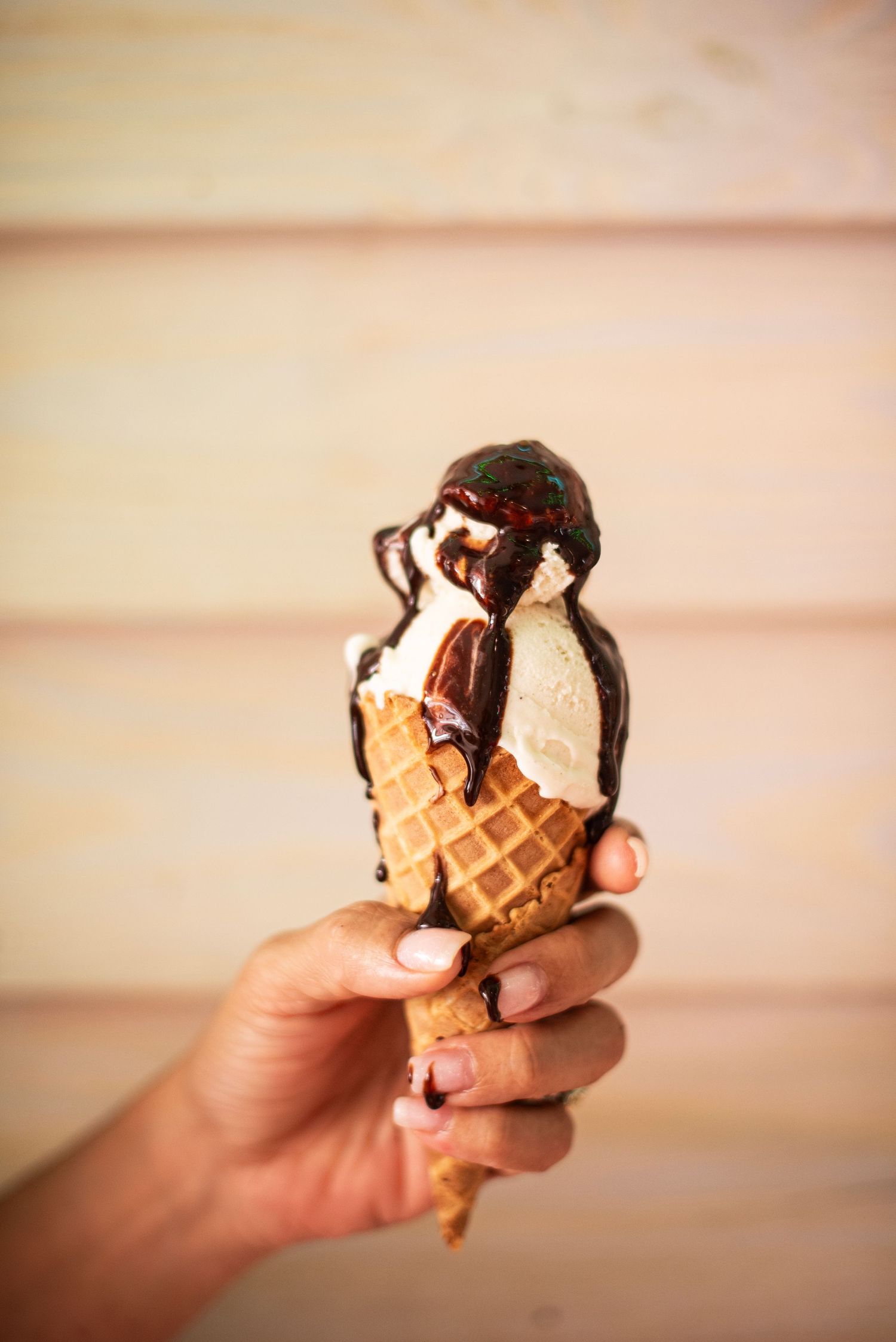 Hand holding a chocolate and vanilla ice cream cone with chocolate drizzle in a sequence of eating shots.