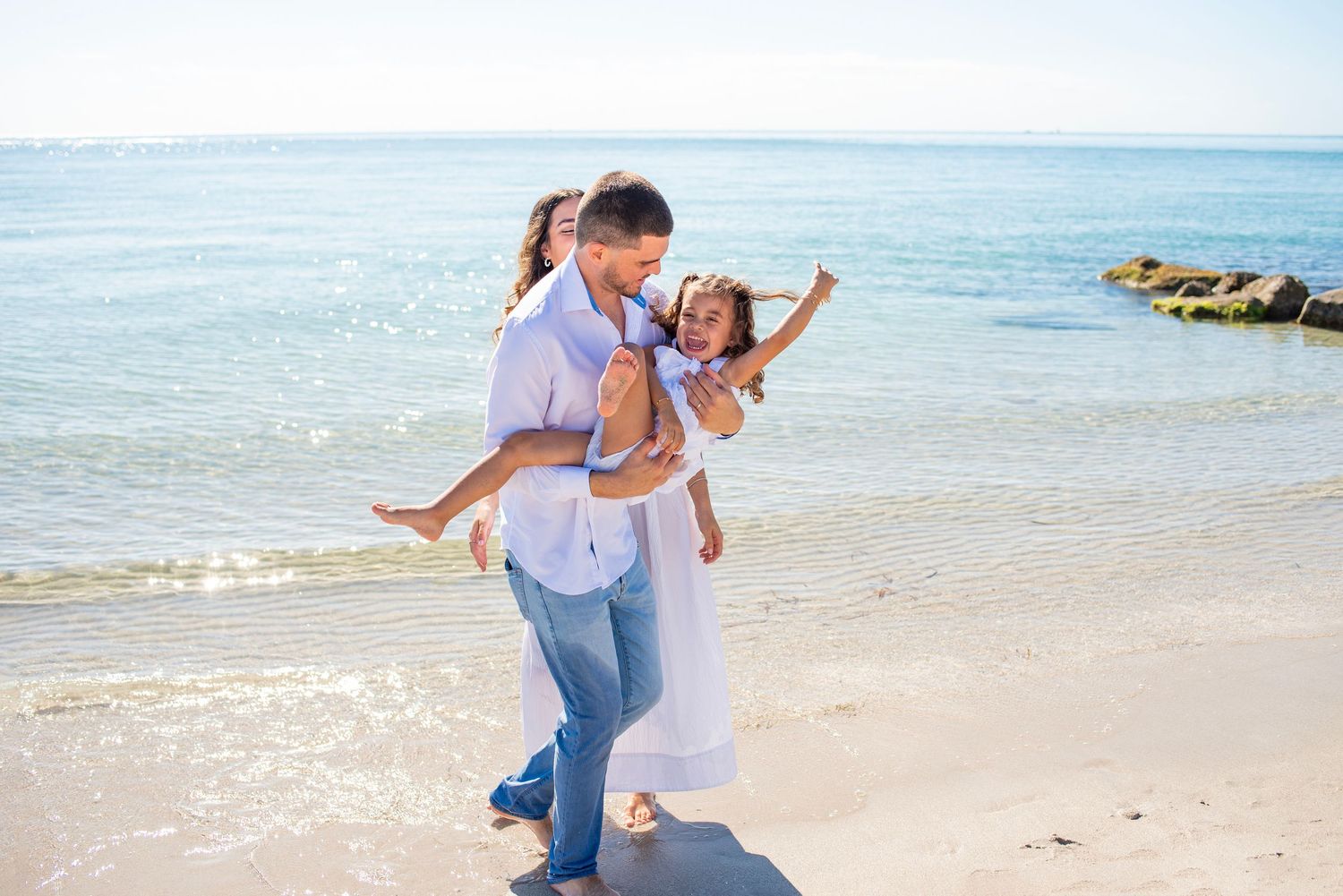 People enjoying a playful moment together on a sunny beach with clear blue water in the background.