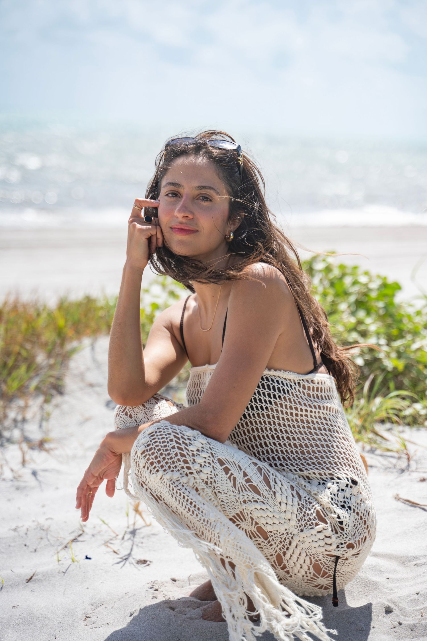 Beach photoshoot featuring crochet dress and flowing hair with ocean waves in background.