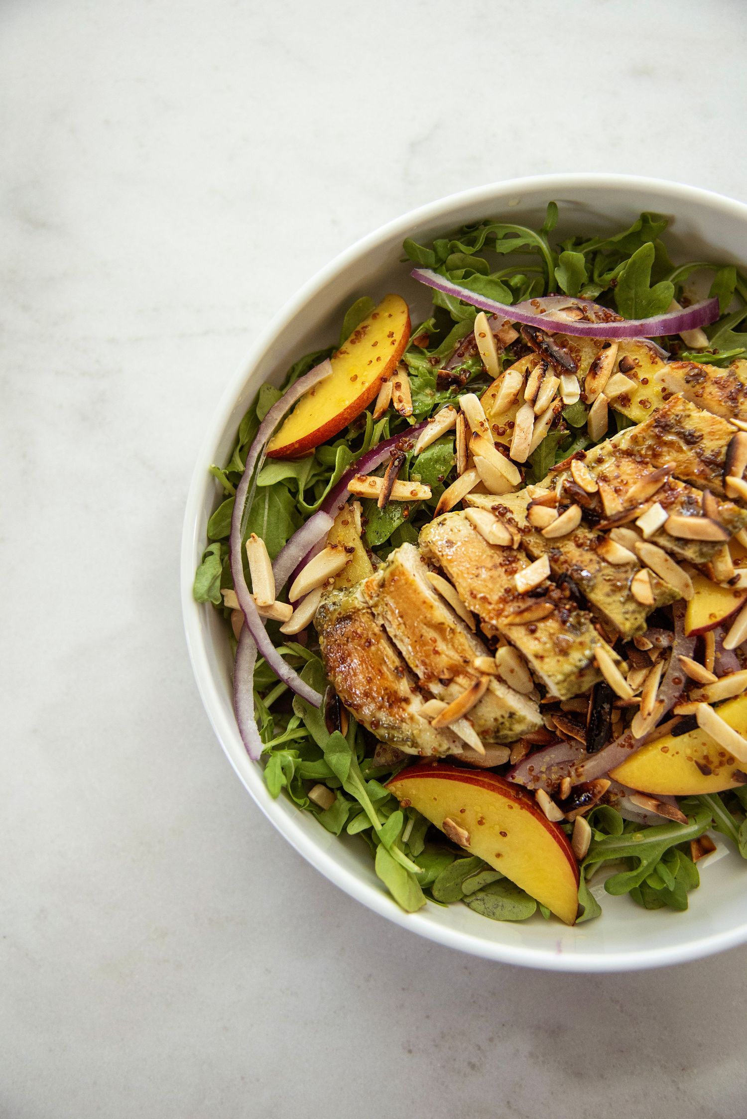 Colorful salad with peaches, almonds and greens in white ceramic bowl.
