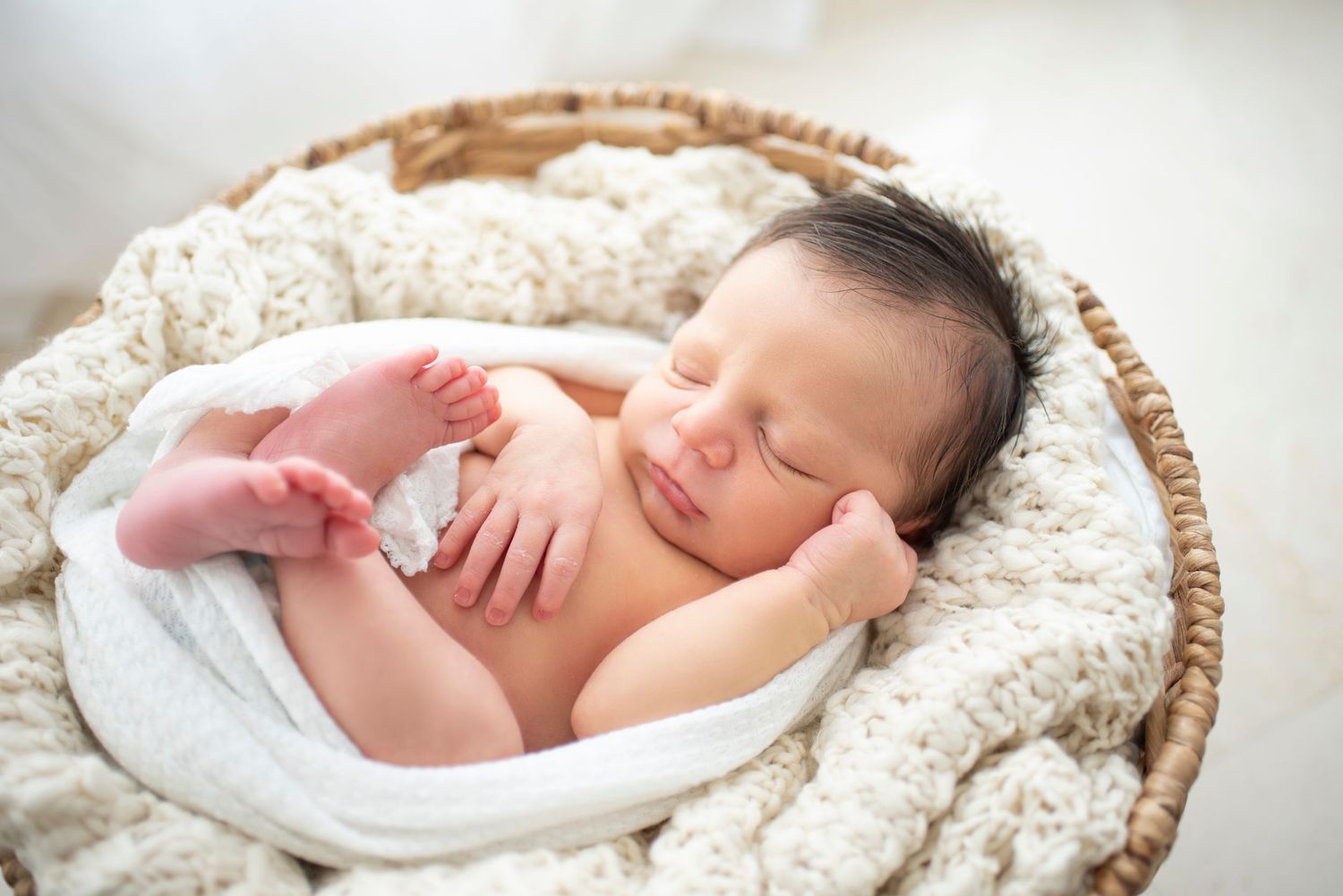 Peaceful newborn baby rests in cozy woven basket during photo session.