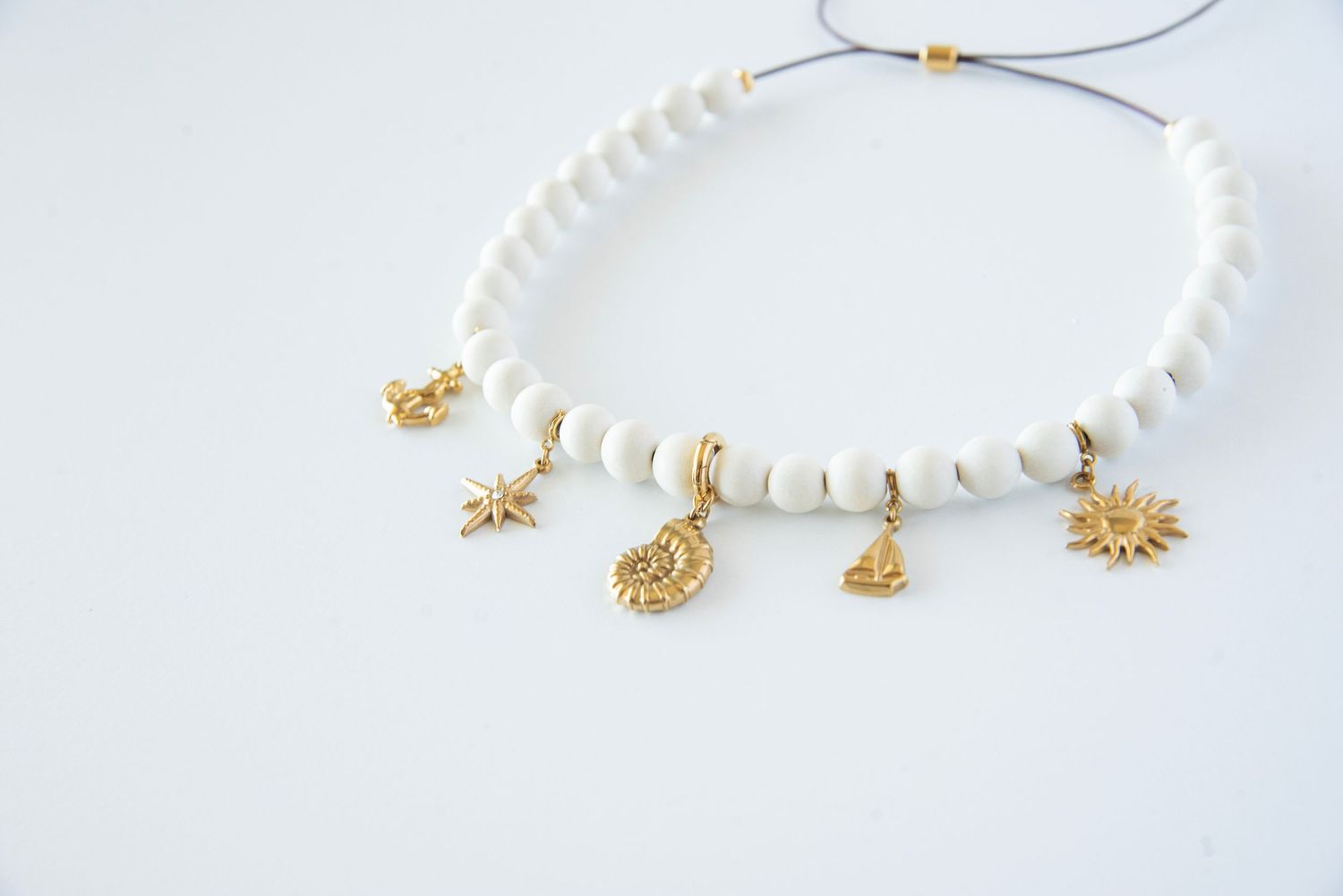 White beaded necklace with gold charms displayed on light background.