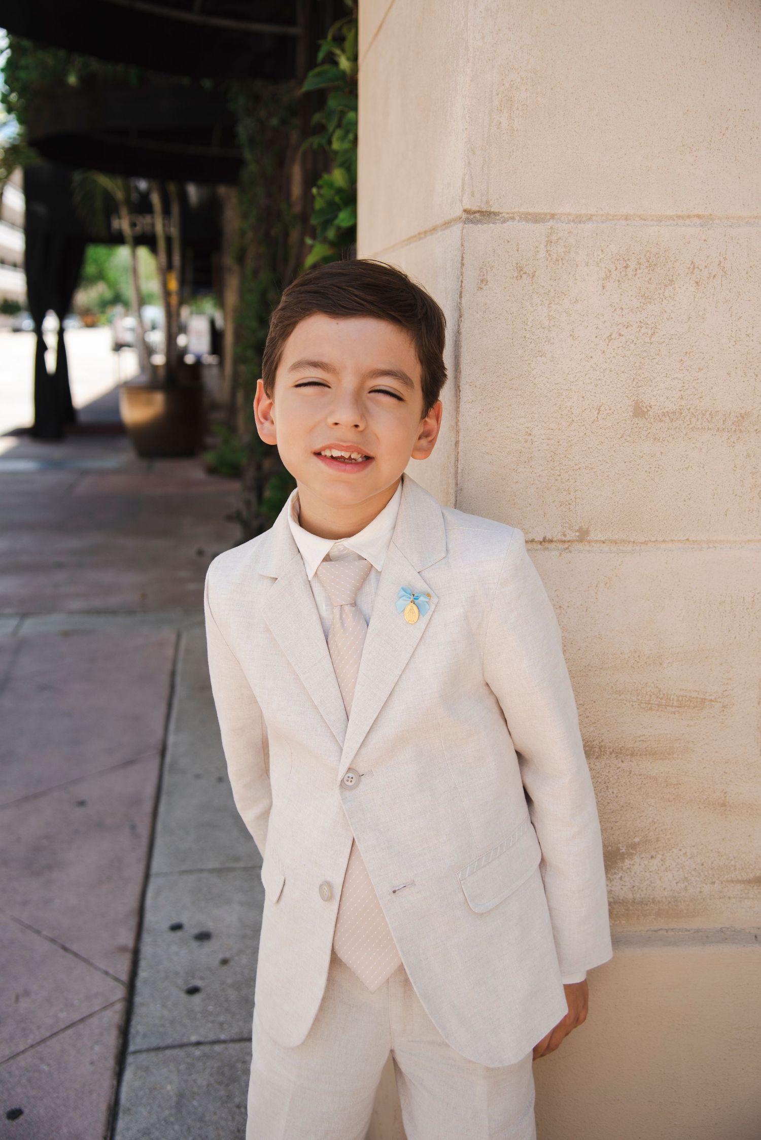 A young attendant in a white suit poses against a stone column.