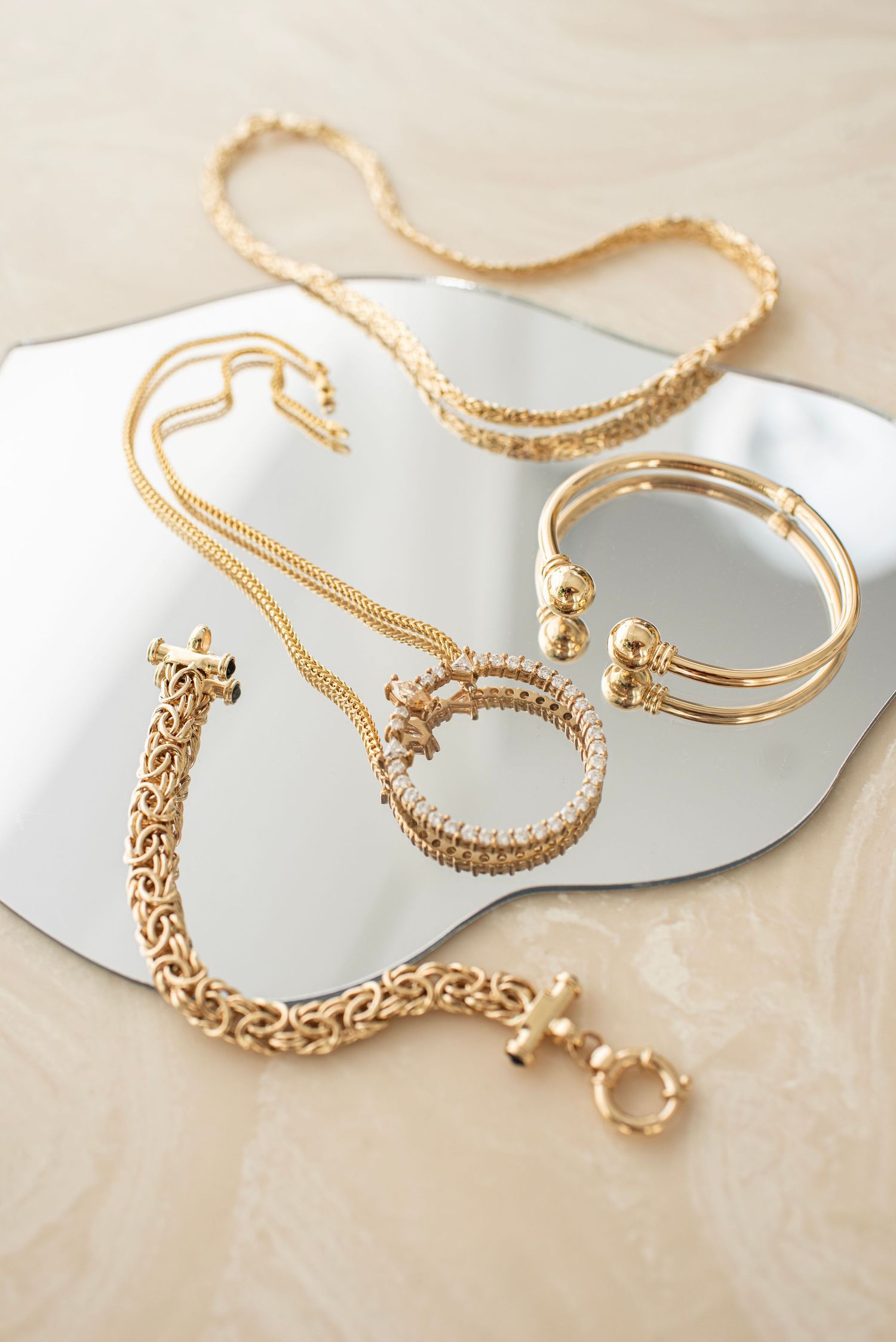 Collection of gold bracelets and chains displayed on reflective surface.