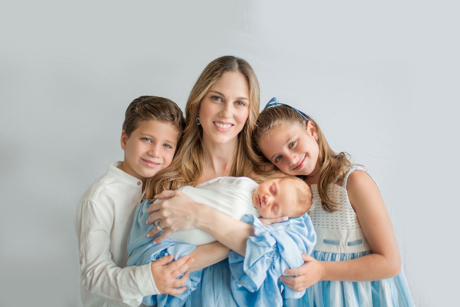 Family members lying together on white bedding in soft natural light.