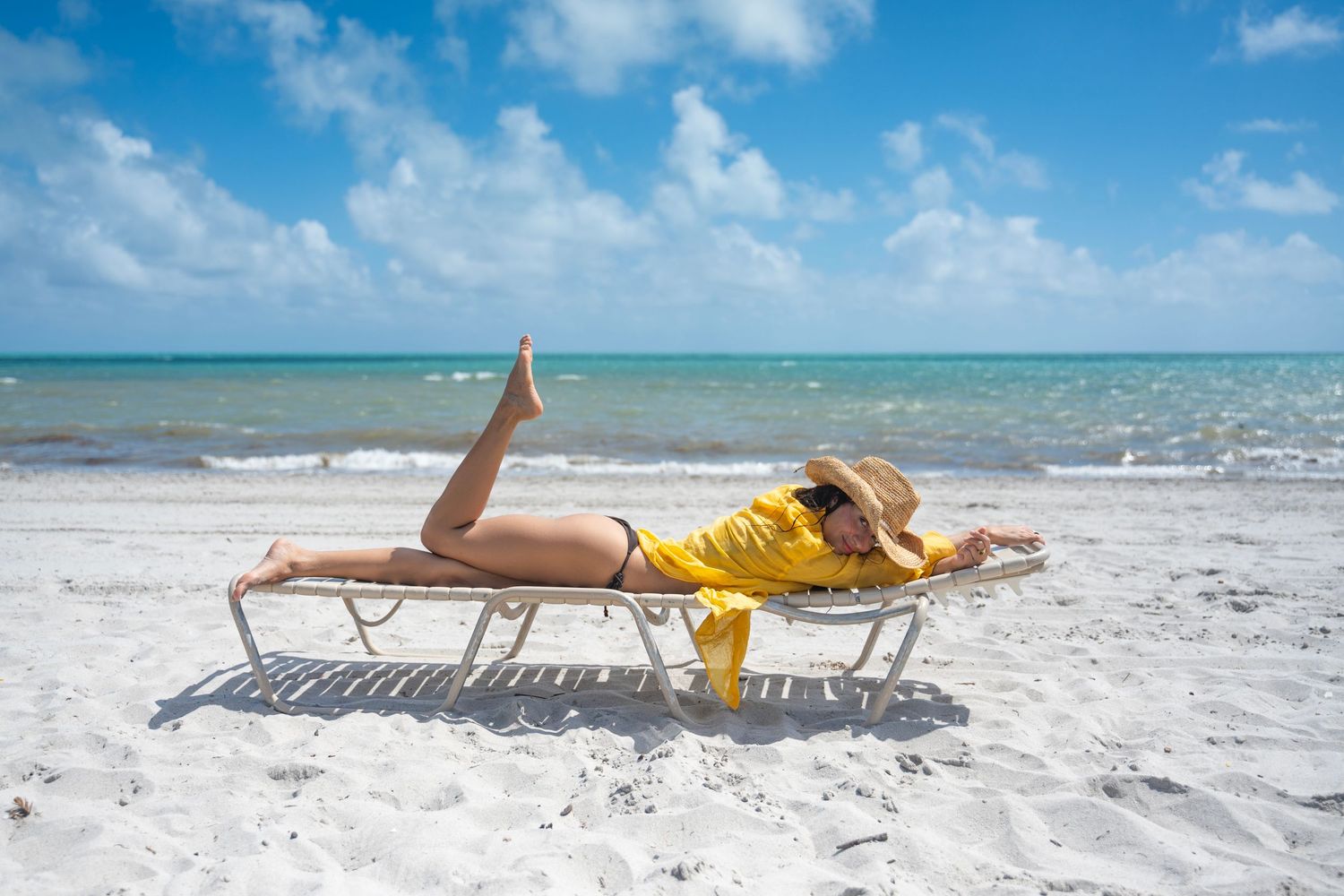 Someone in a yellow swimsuit relaxes on a beach chair along the turquoise waters of a tropical beach.