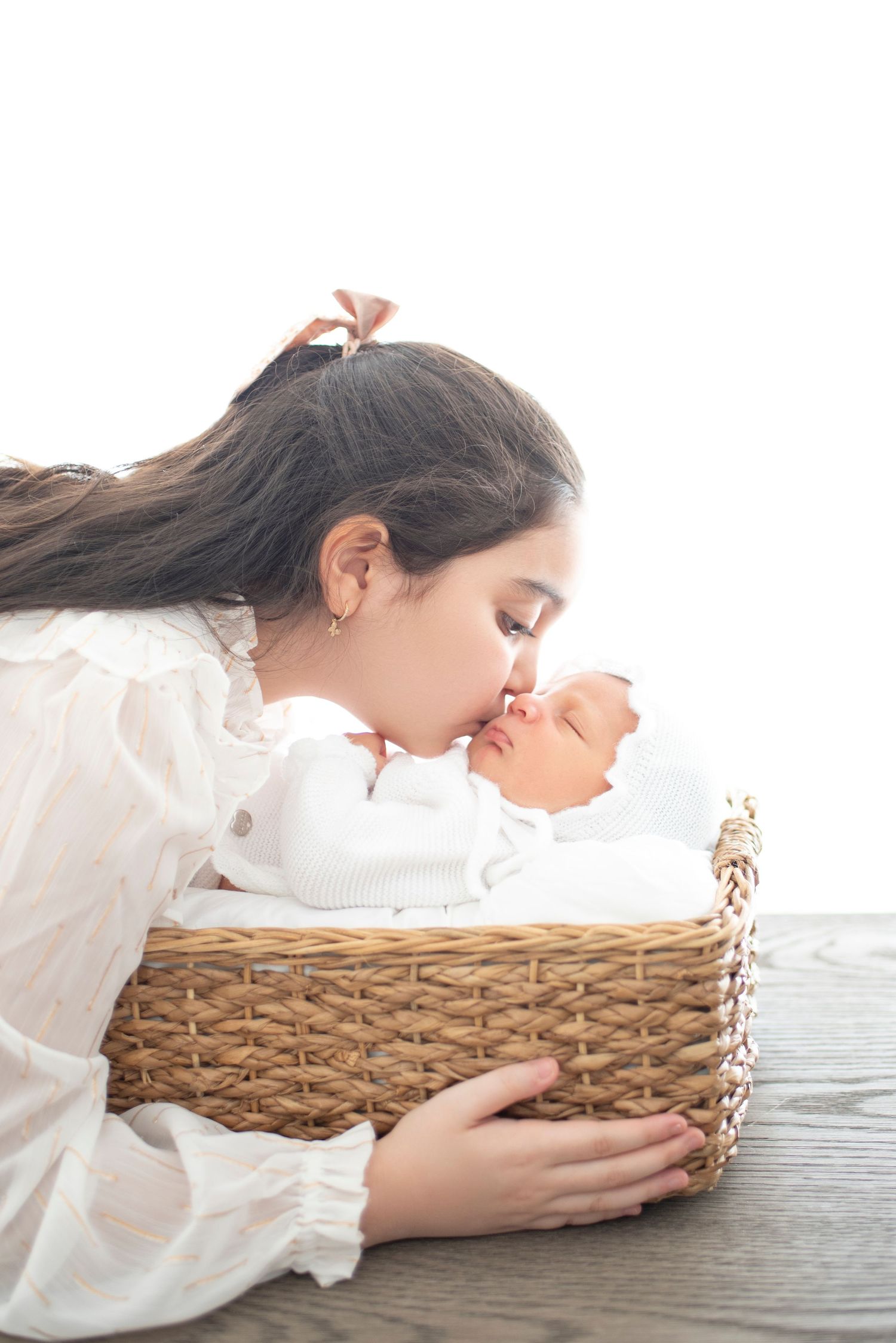 Artistic newborn photography with baby in woven basket against white backdrop.