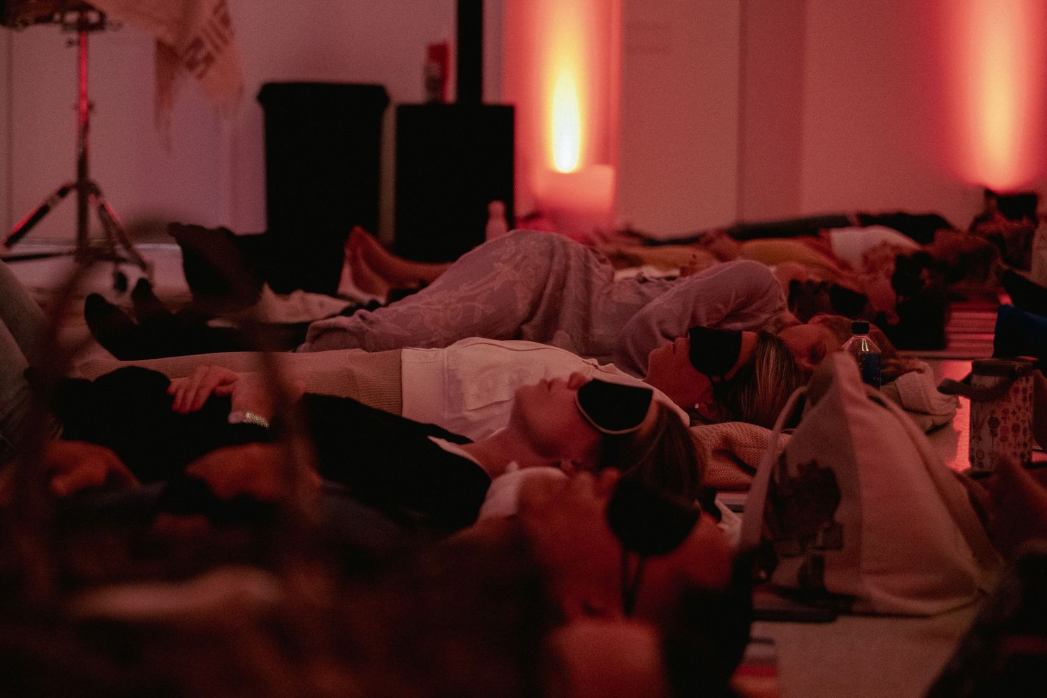 Group of people lying on the floor in a dimly lit room with warm pink ambient lighting during a relaxation event.