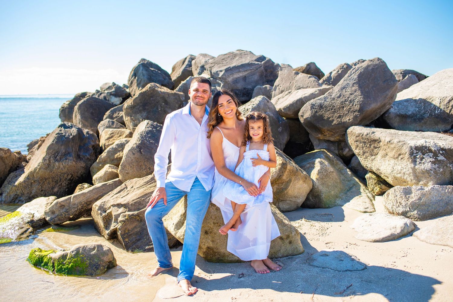 A joyful moment captured on a rocky beach with white attire and ocean waves in the background.
