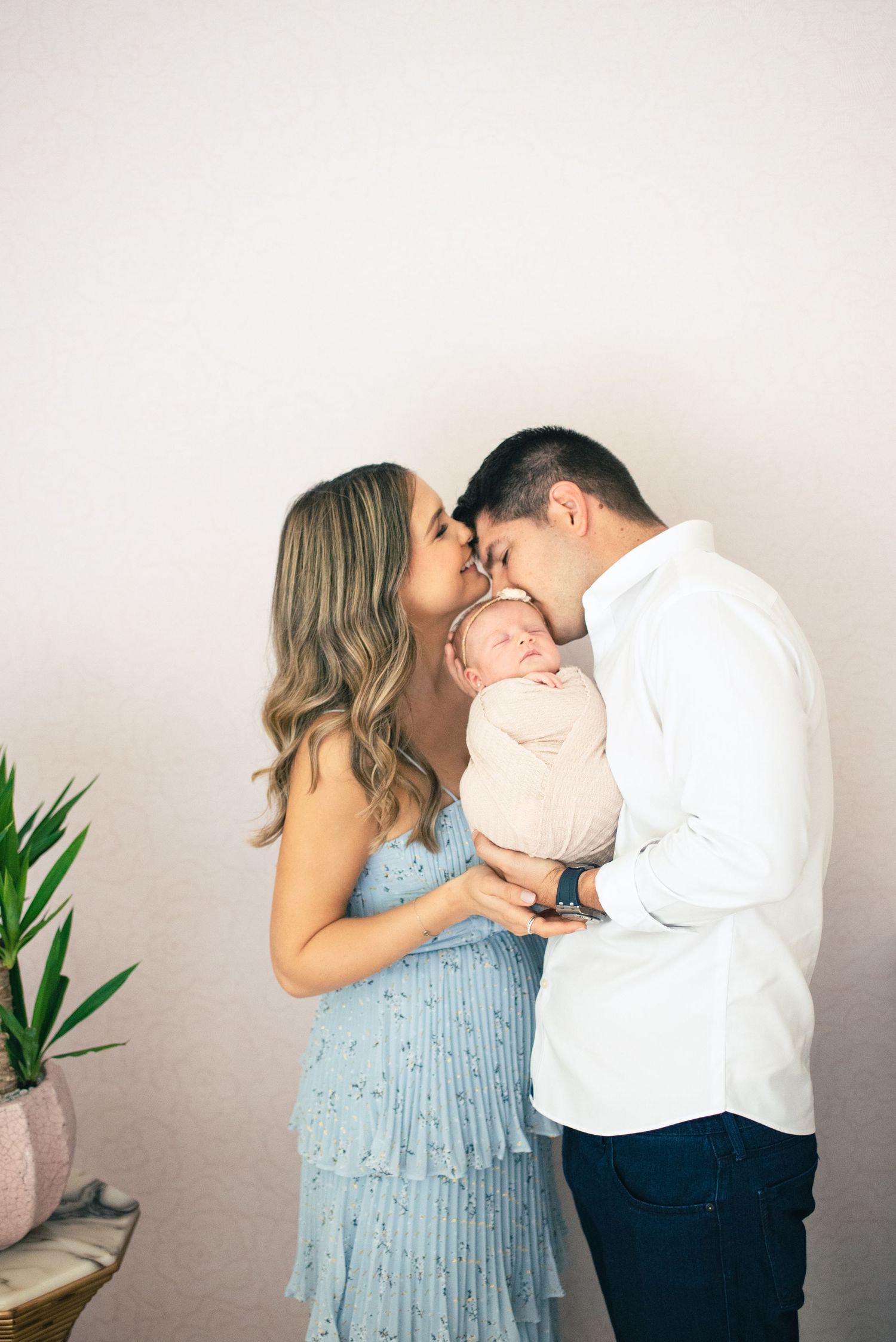 A couple in light blue and white outfits share tender moments in a series of romantic photos against a neutral wall.