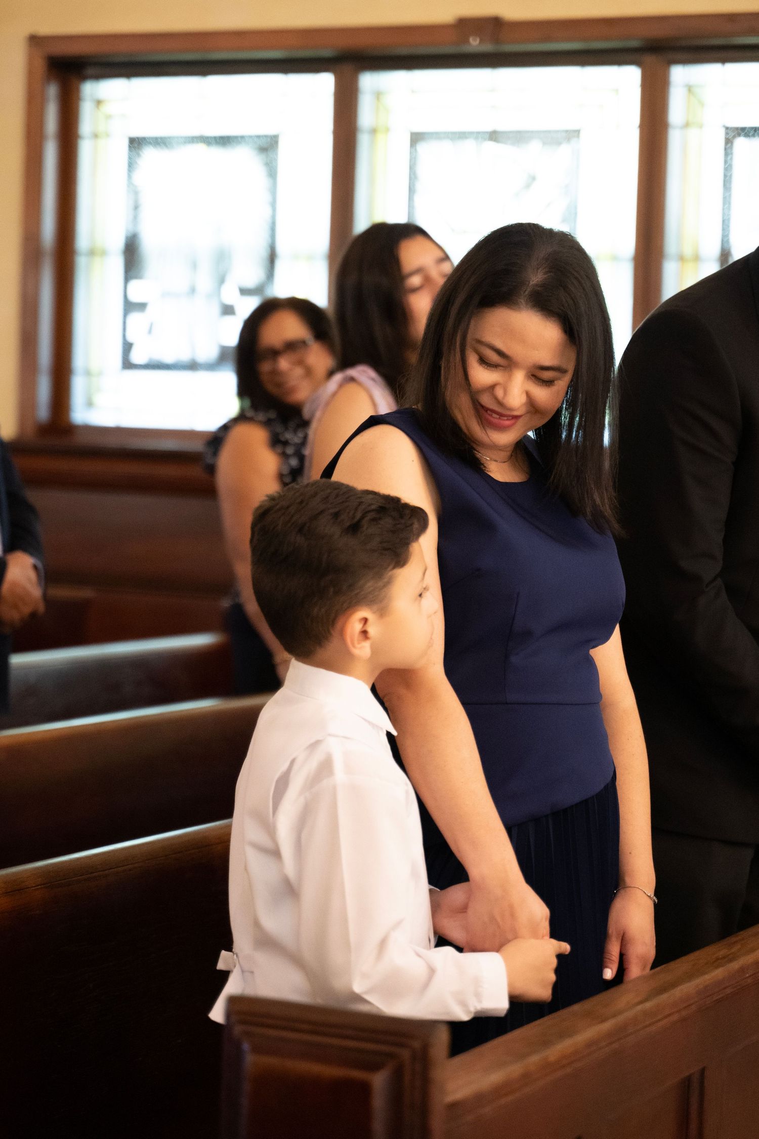 A woman in a navy dress smiles warmly at a young boy in a white shirt inside a church.