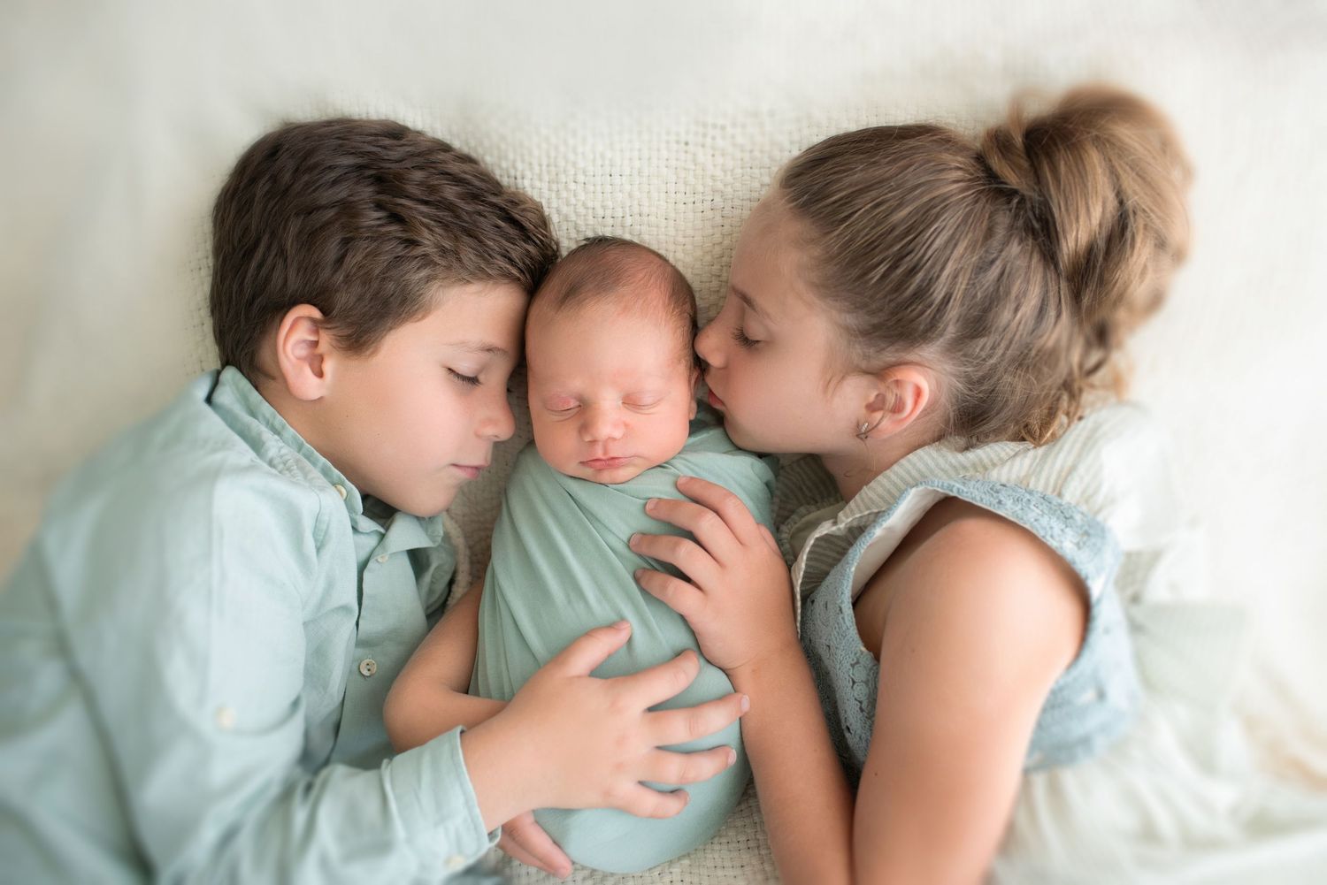 Family members cuddling together on white bedding in studio.