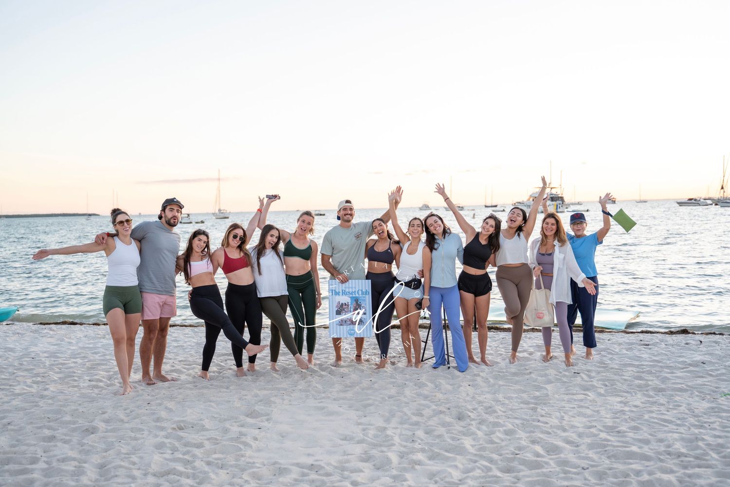 Group of friends standing in a line on the beach at sunset posing for a photo.