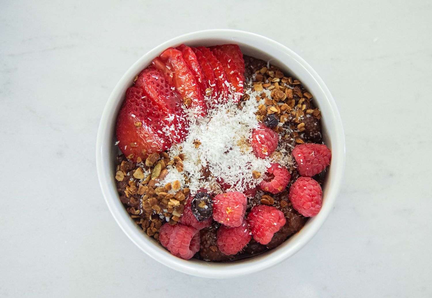 Bowl of fresh raspberries topped with chocolate crumble and coconut flakes.
