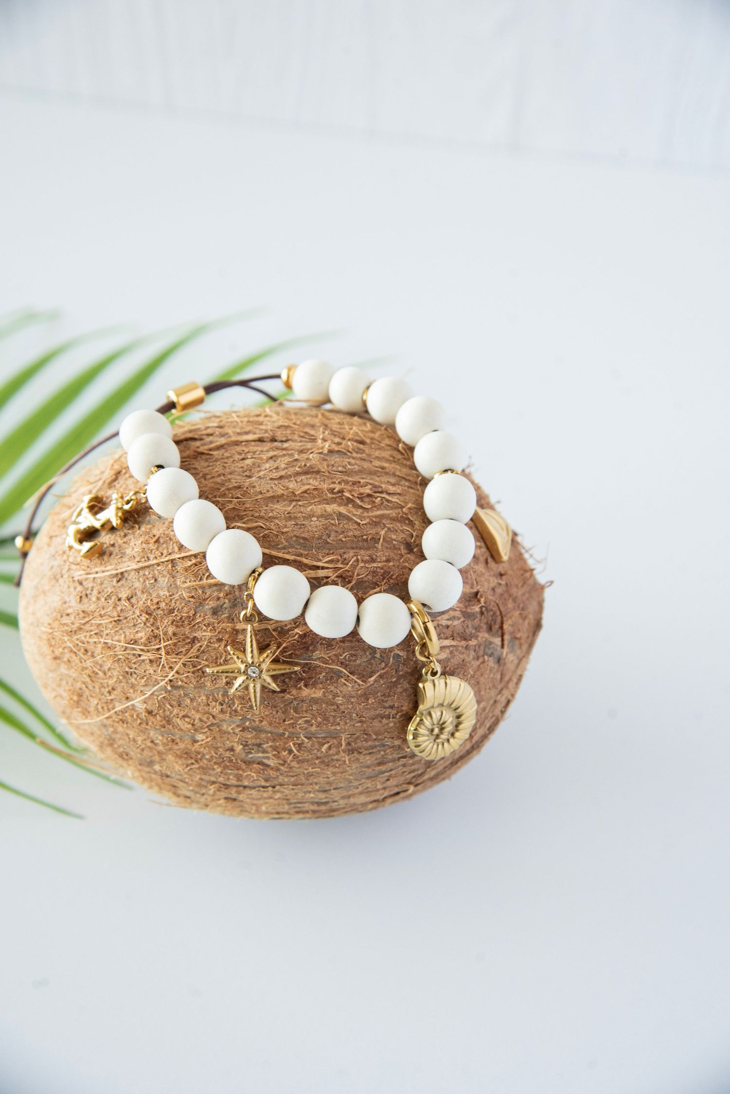 White beaded necklace with gold charms displayed on coconut shell against light background.