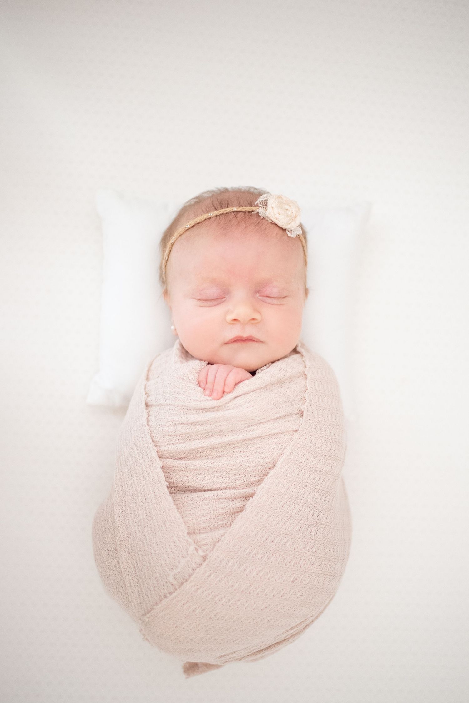 A peaceful sleeping newborn baby swaddled in soft pink fabric against a white background.