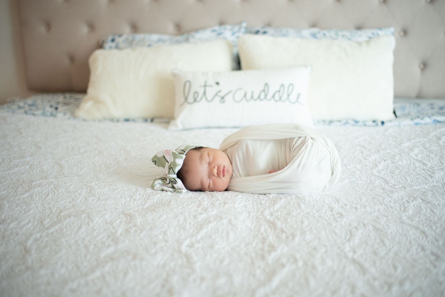 Newborn baby wrapped in white blanket sleeping peacefully on soft white textured bedding.