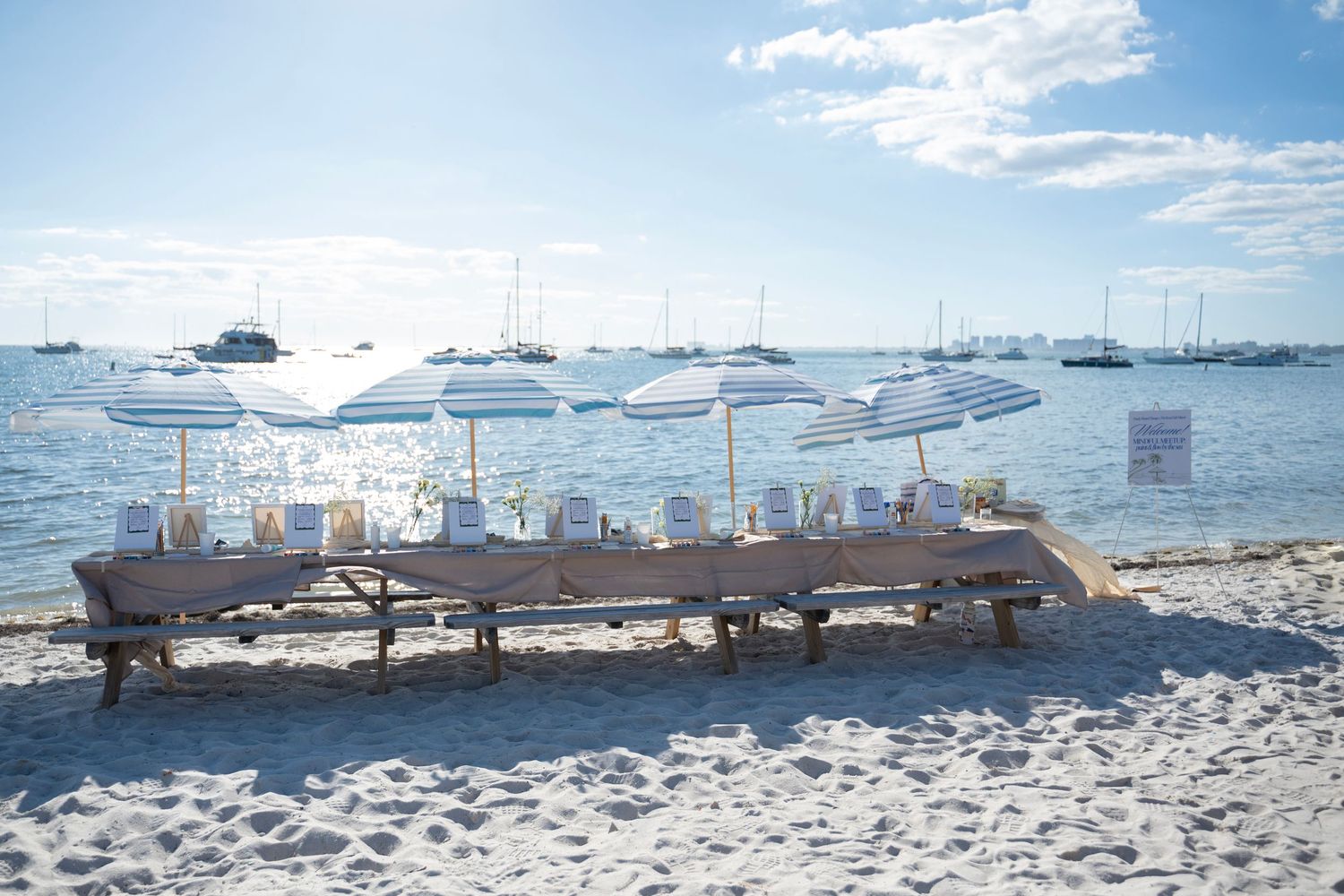 Panoramic view of a beach with white umbrellas, lounge chairs and boats dotting the shoreline against a blue sky.