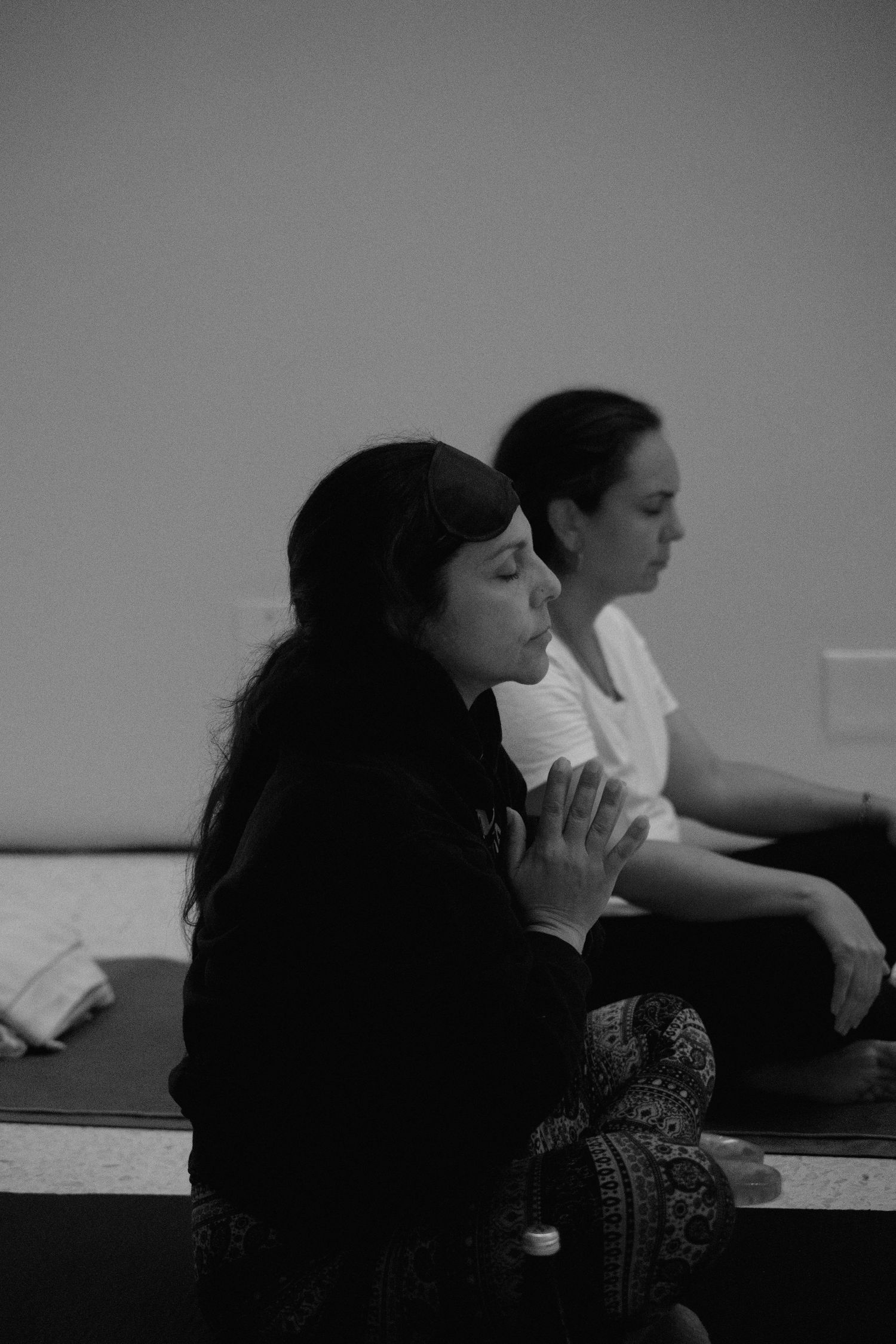 Two women sit in meditation poses during a yoga class, captured in black and white photography.