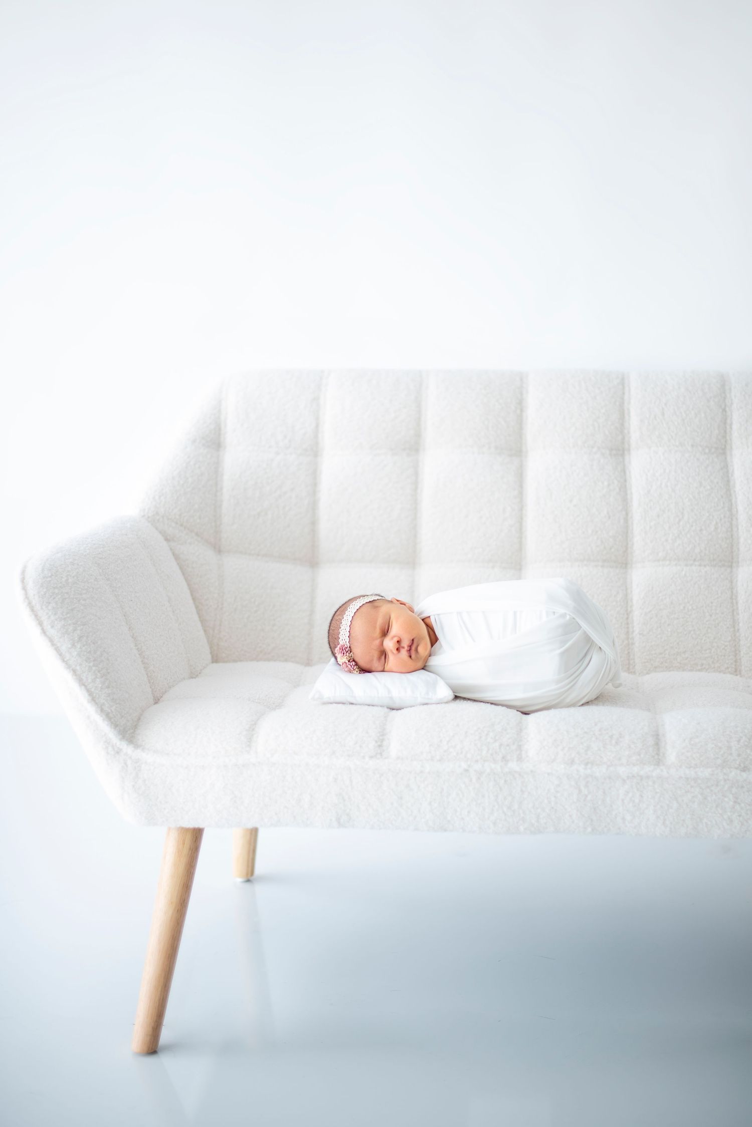 A white modern sofa with wooden legs against a light blue background in a minimalist setting.