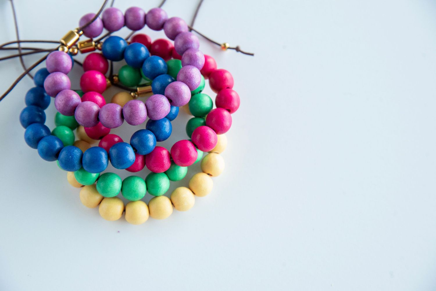Colorful beaded bracelets arranged in a gradient pattern with pink, blue, and yellow wooden beads.