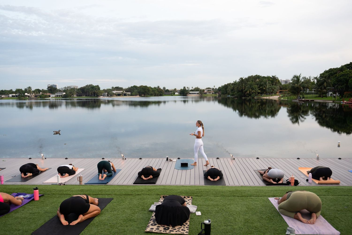 Group yoga session on lakeside dock during sunset.