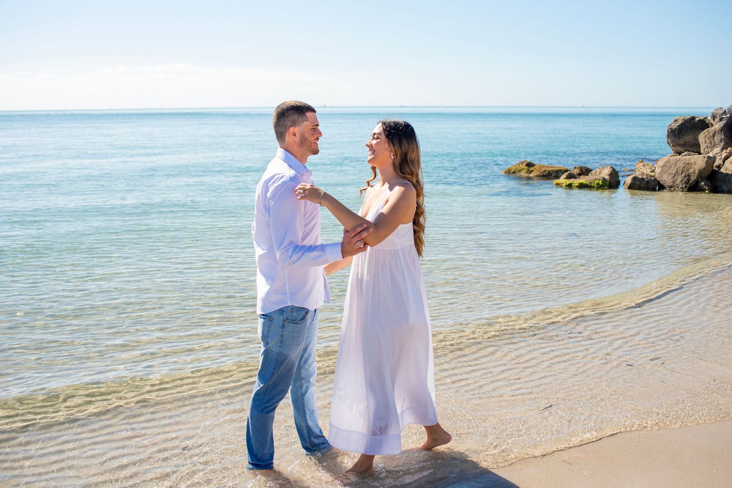 A couple shares a romantic moment on a tropical beach with turquoise waters and soft sand in the background.
