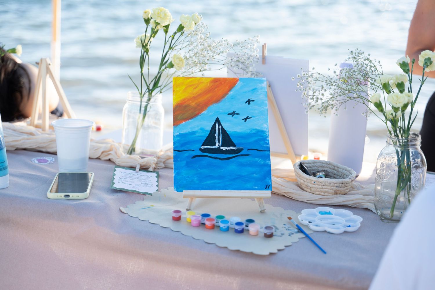White flowers in vases decorate a bright coastal-themed table setting with blue accents and sailboat artwork.