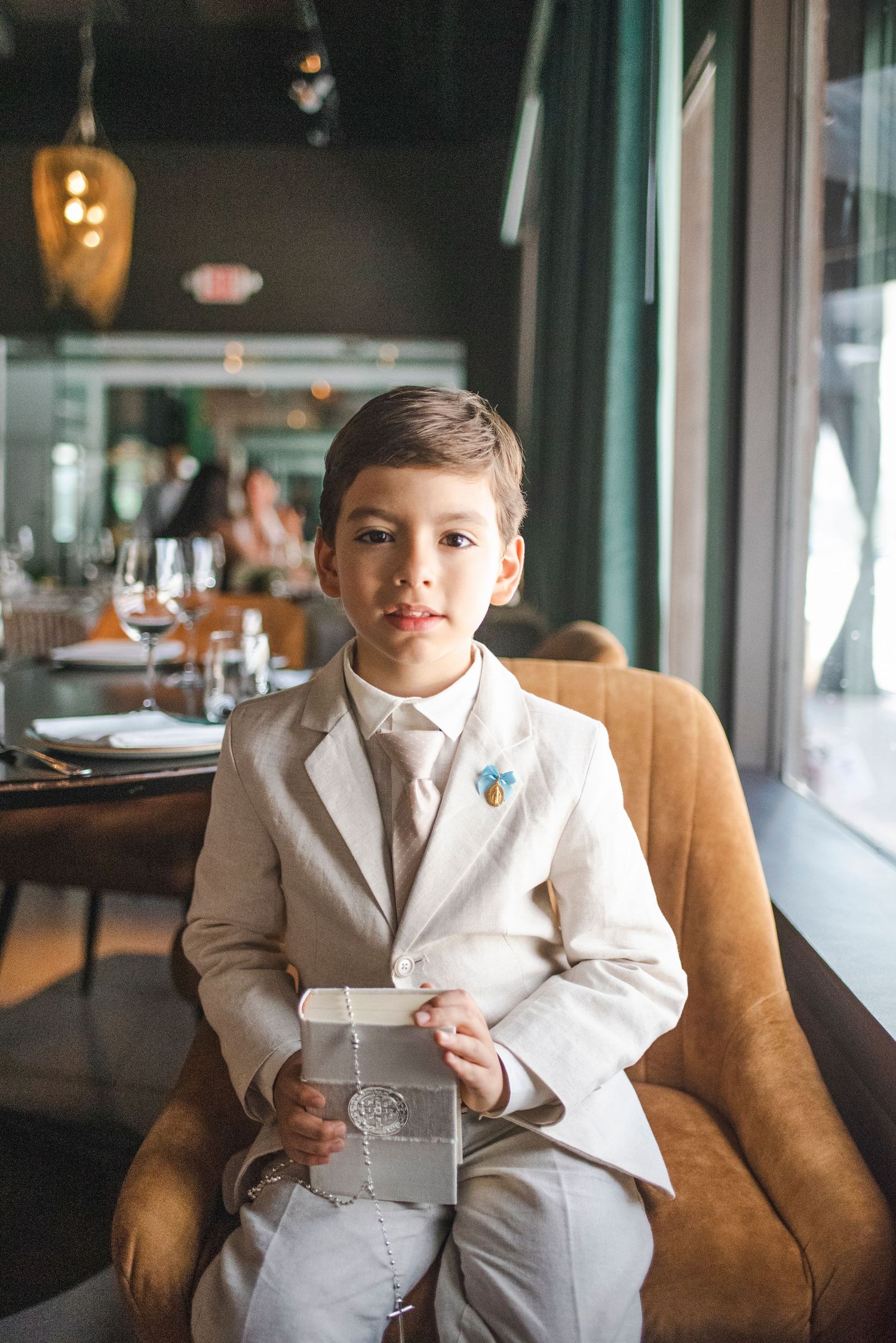 Young person in white suit sitting on brown leather couch in restaurant setting.