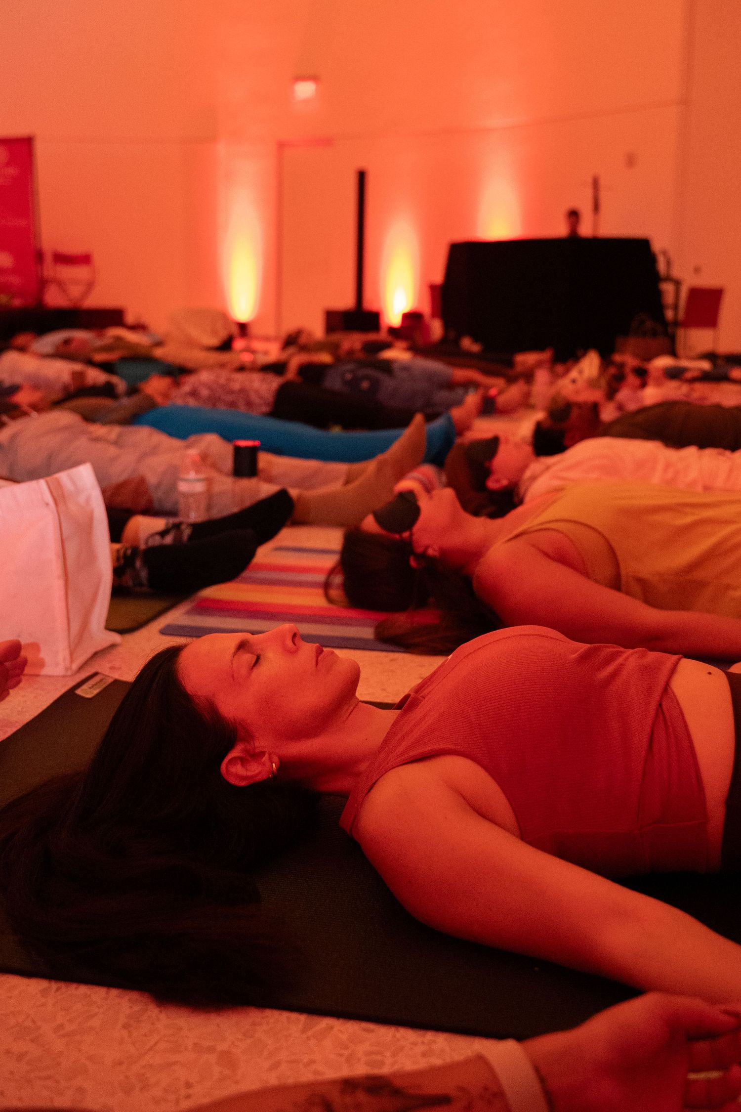 People lying on yoga mats in savasana pose during a relaxation session in an orange-lit wellness studio.