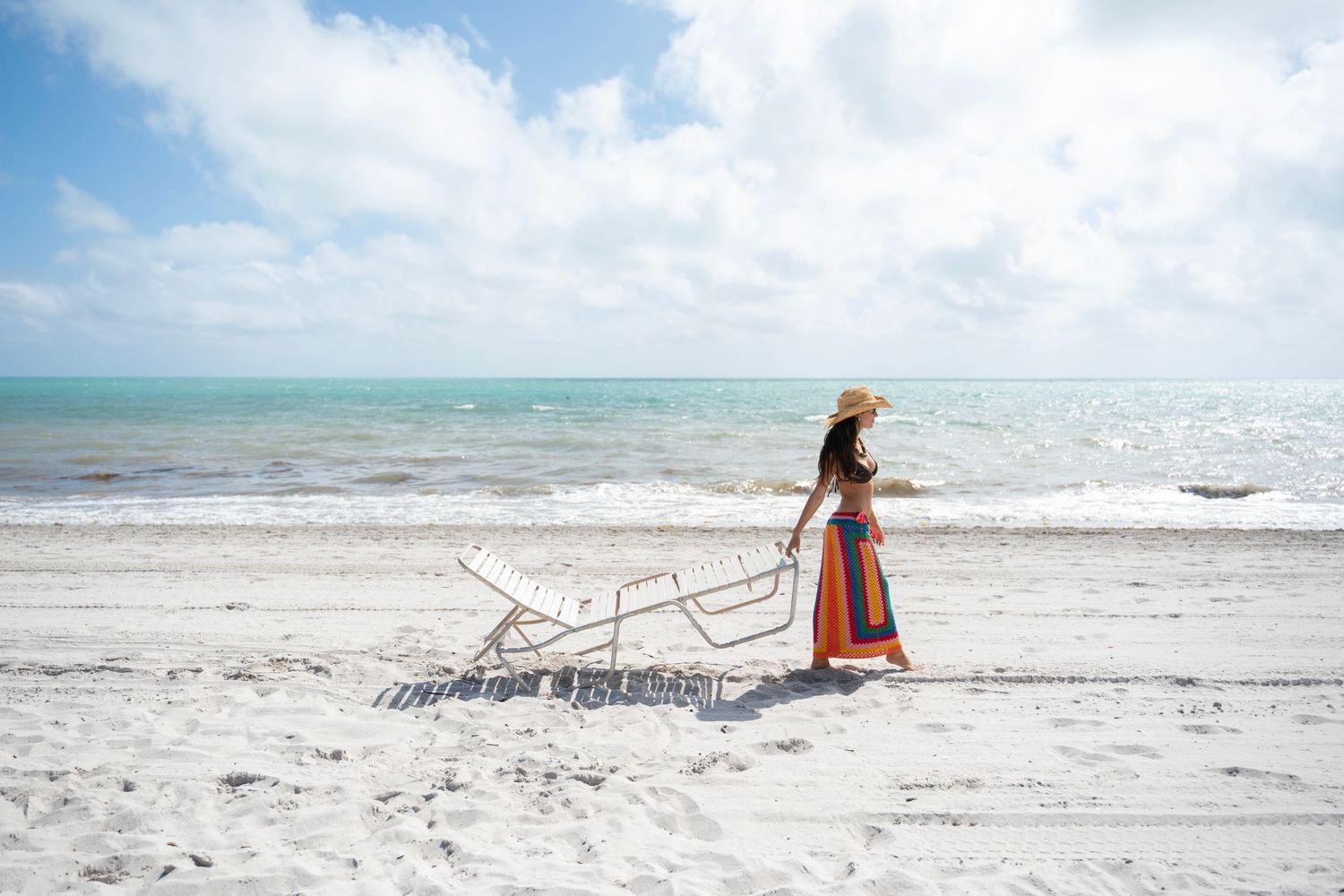 A serene beachfront panorama shows a lone figure reading on a white sandy shore with turquoise waters and driftwood.