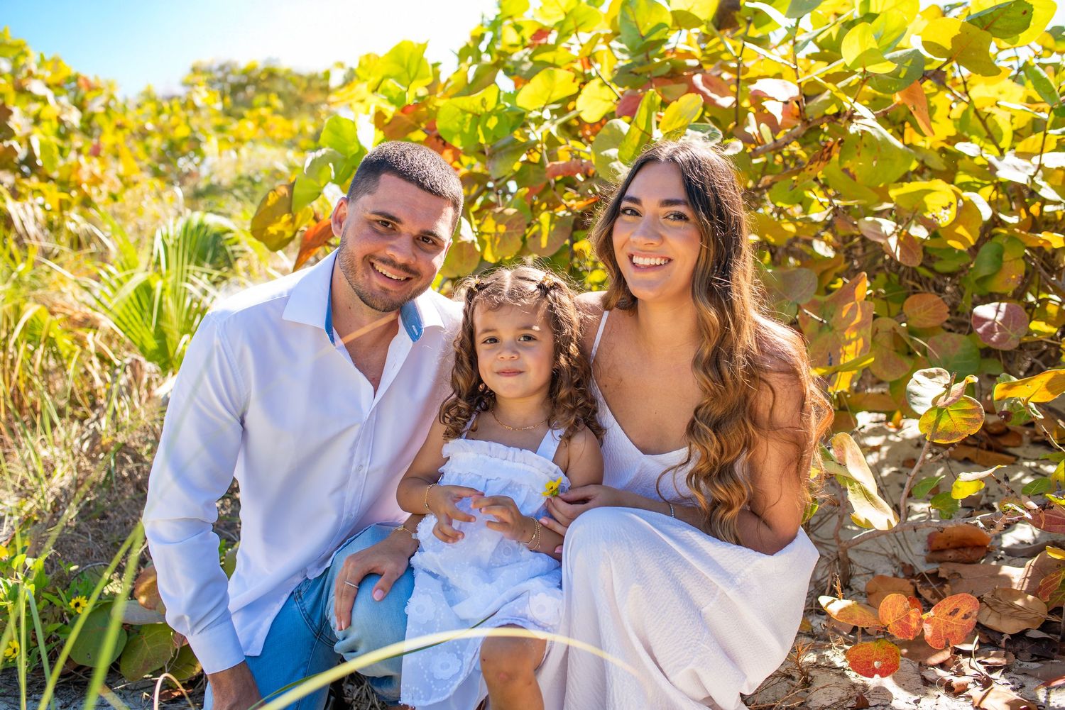 A family laughs together while sitting among autumn grape vines on a sunny day.