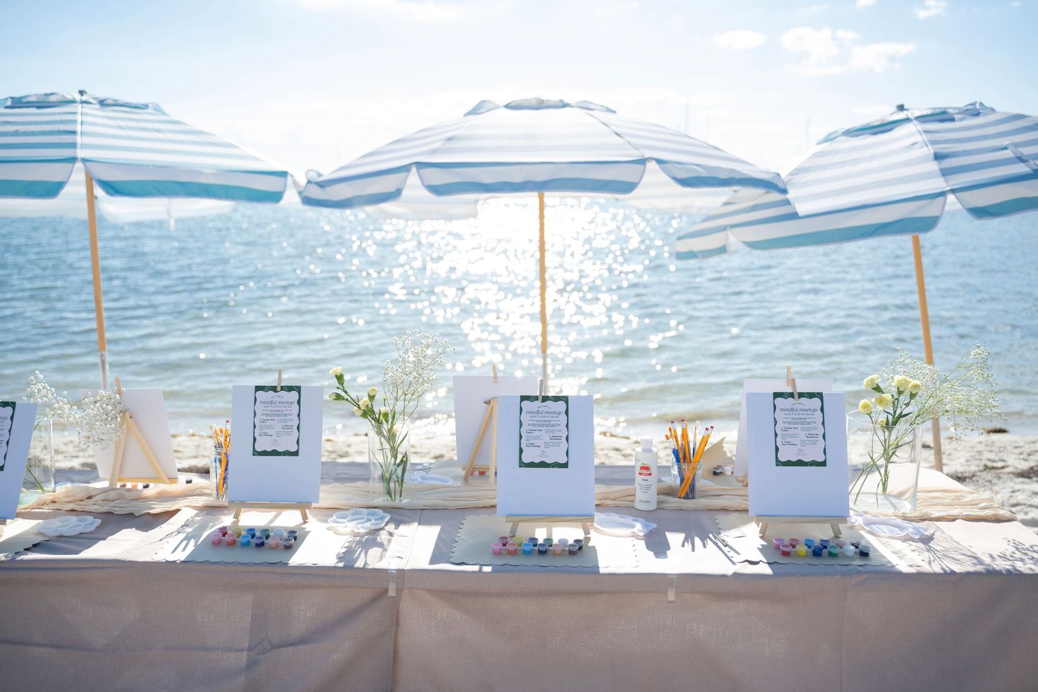 A row of white beach umbrellas and lounge chairs line the shore with calm blue ocean waters in the background.