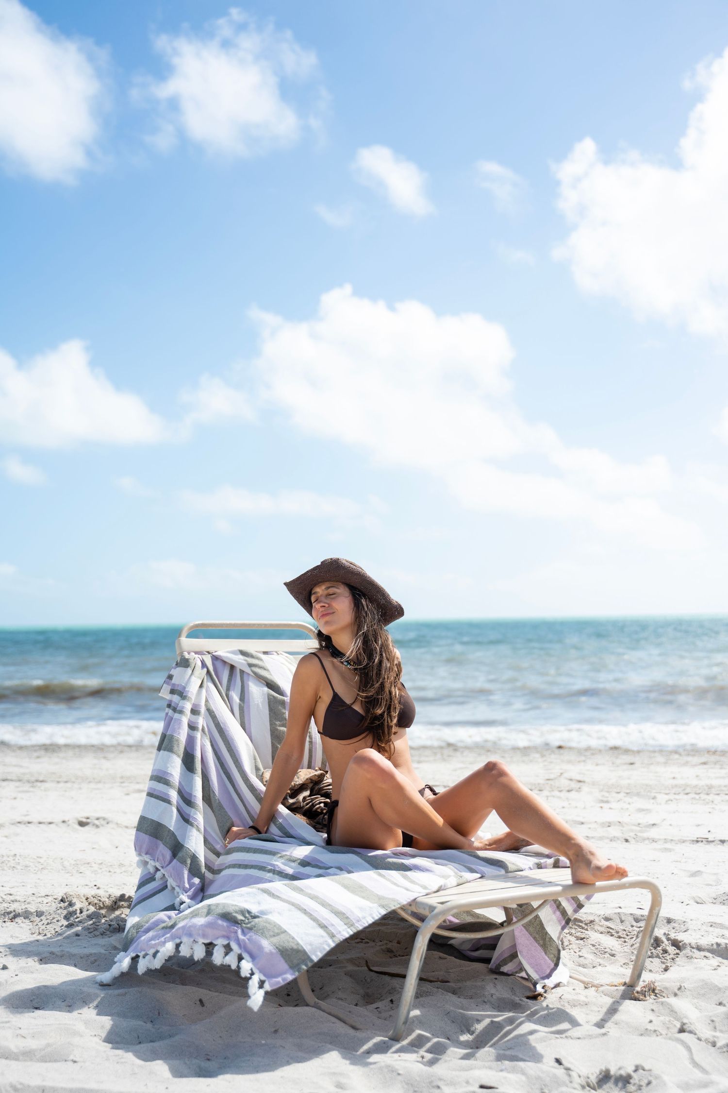A person relaxes on a striped beach towel while enjoying a sunny day at a tropical beach with turquoise waters.