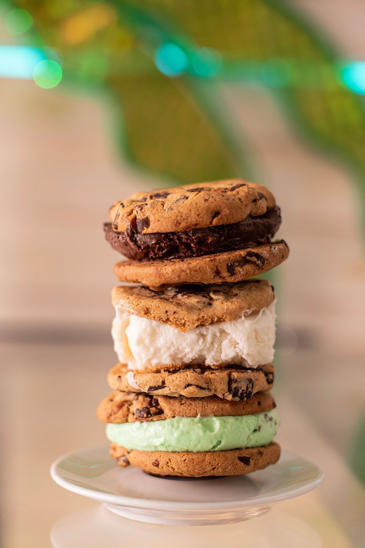 Stack of gourmet ice cream sandwiches with chocolate chip cookies and various colorful fillings on a white plate.