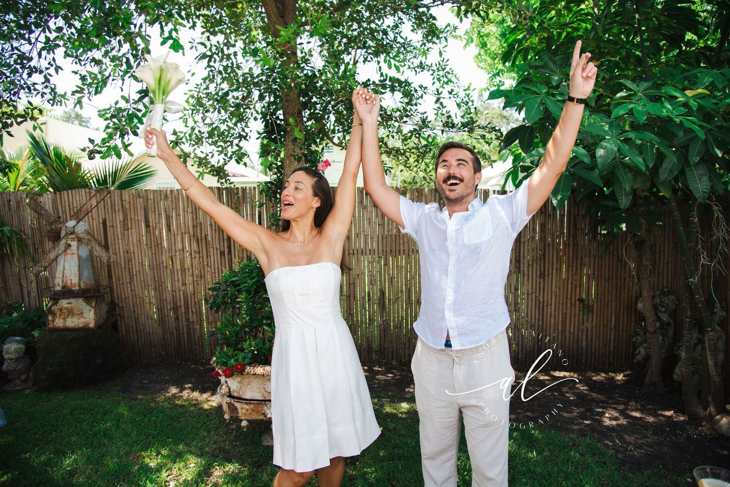 People celebrating with raised arms in a sunny backyard garden setting.