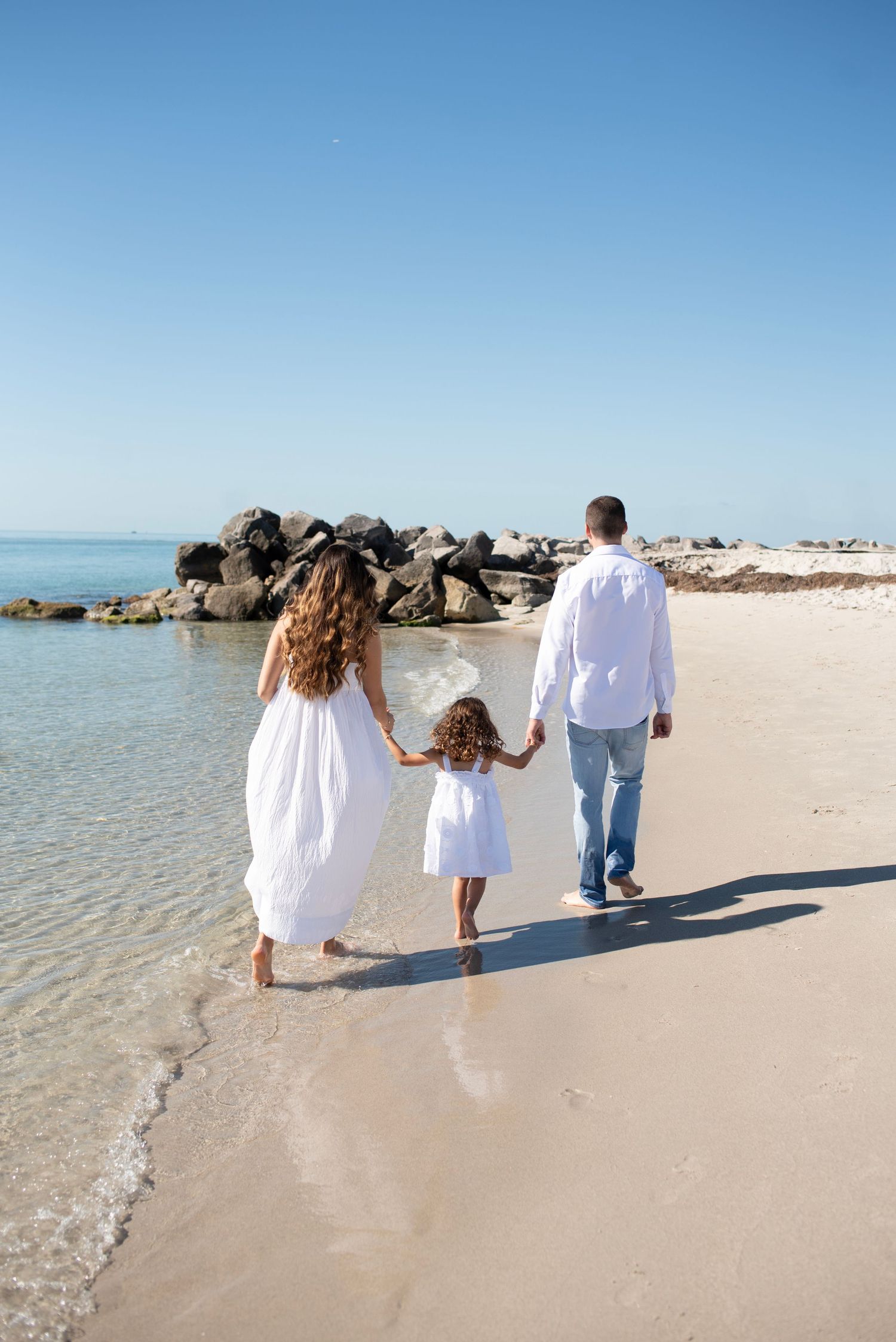 A family walks together along a pristine white sand beach with crystal clear turquoise waters on a sunny day.