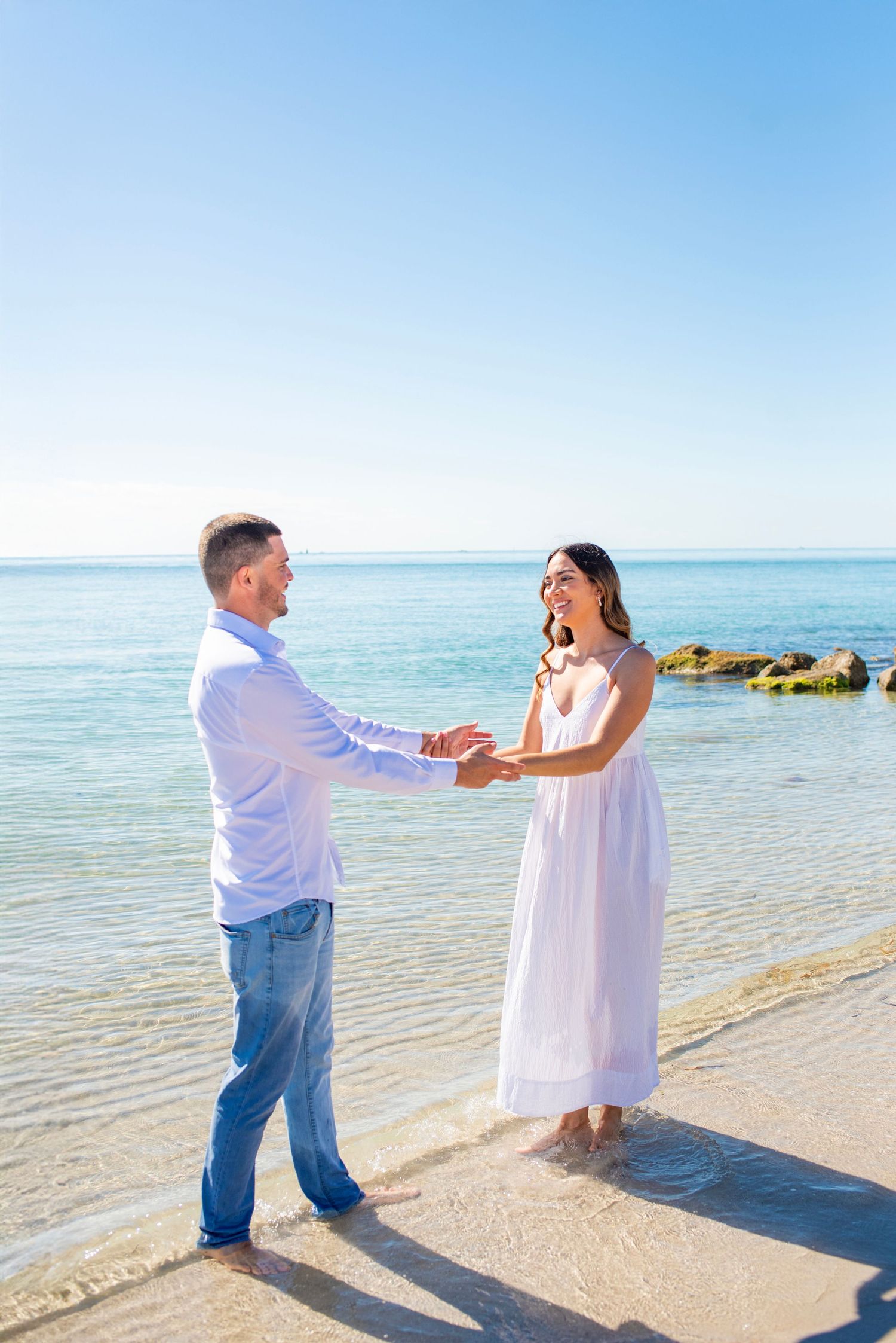 A couple dances together on a sunny beach with turquoise waters and white sand in the background.