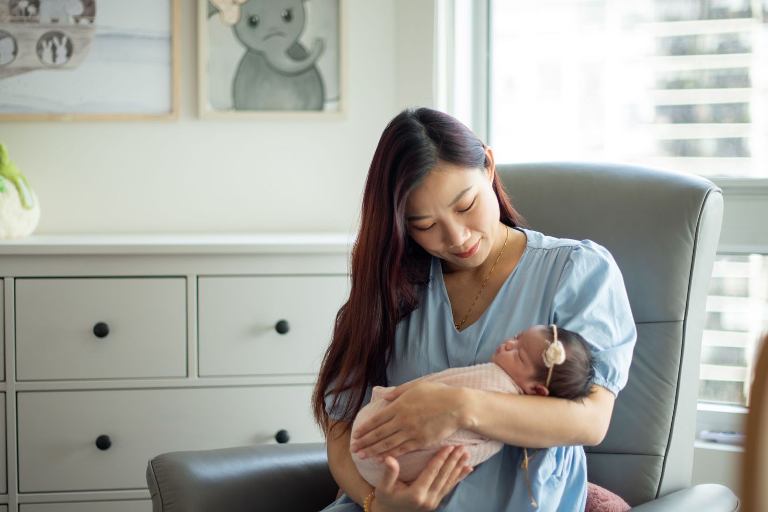 A mother holds and comforts a crying baby in a bright, modern nursery room with white furniture.
