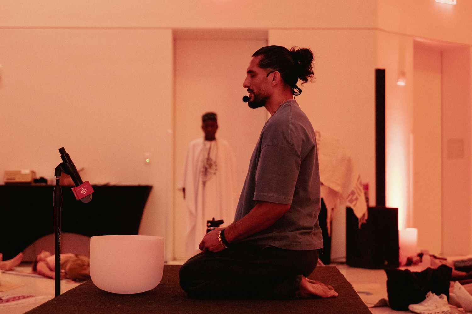 Man meditating in lotus pose beside crystal singing bowls during a sound healing session in a warm studio.