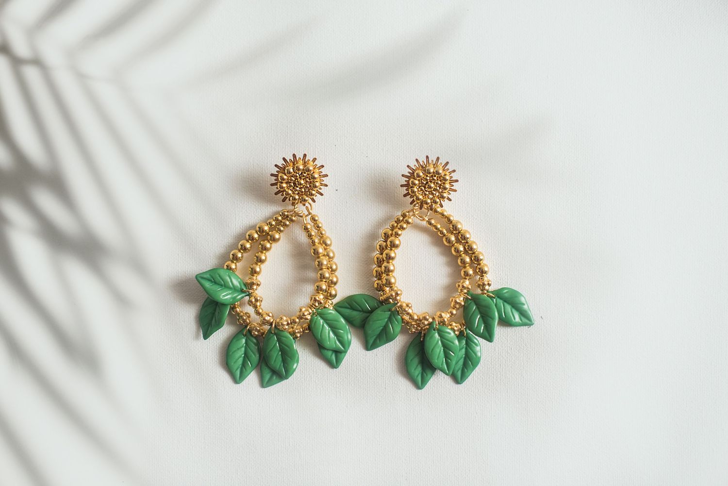 Delicate gold and green leaf-shaped stud earrings with crystal accents displayed in multiple angles on white surface.