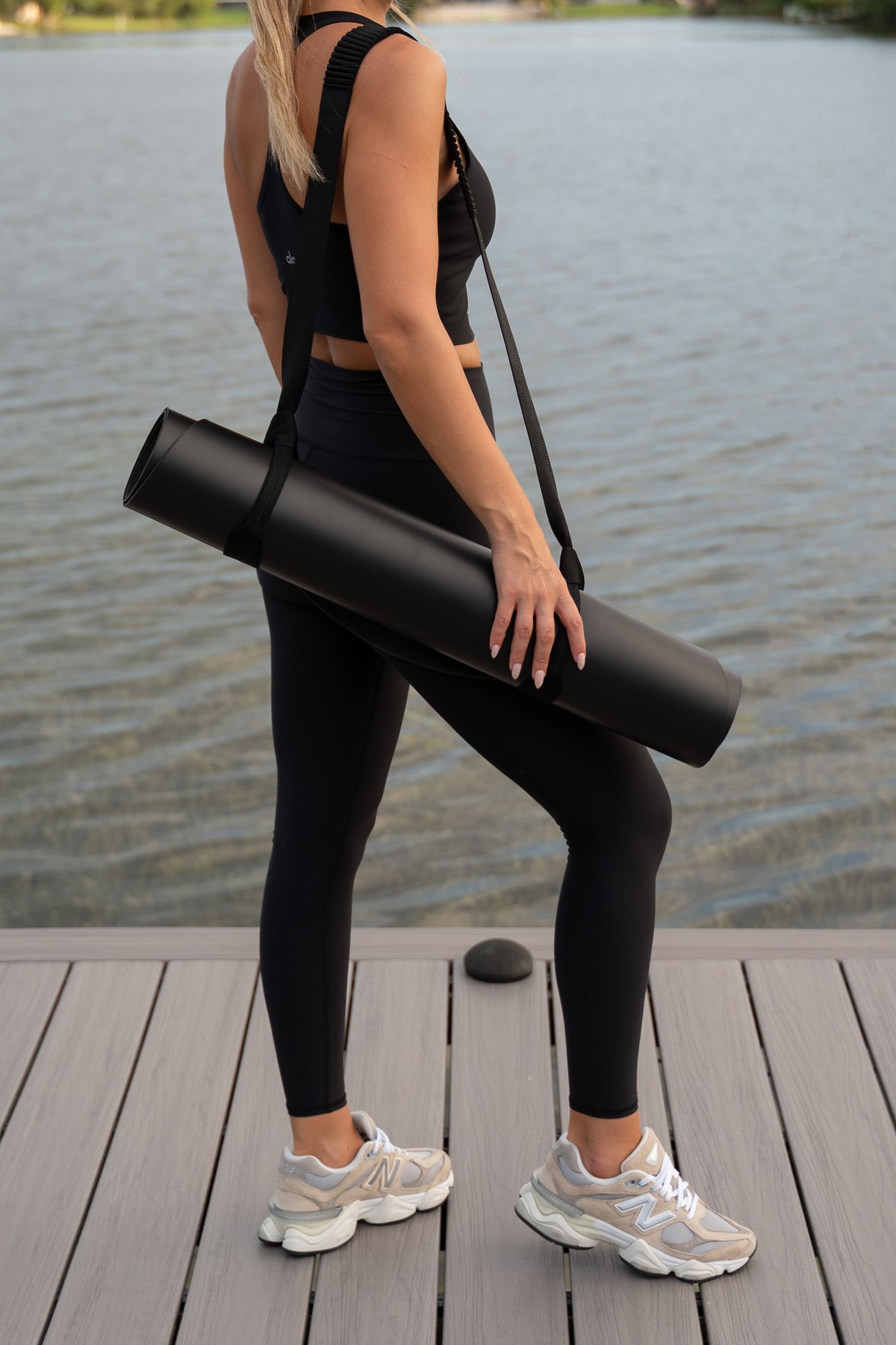 Side view of someone carrying a black yoga mat on a waterfront deck.
