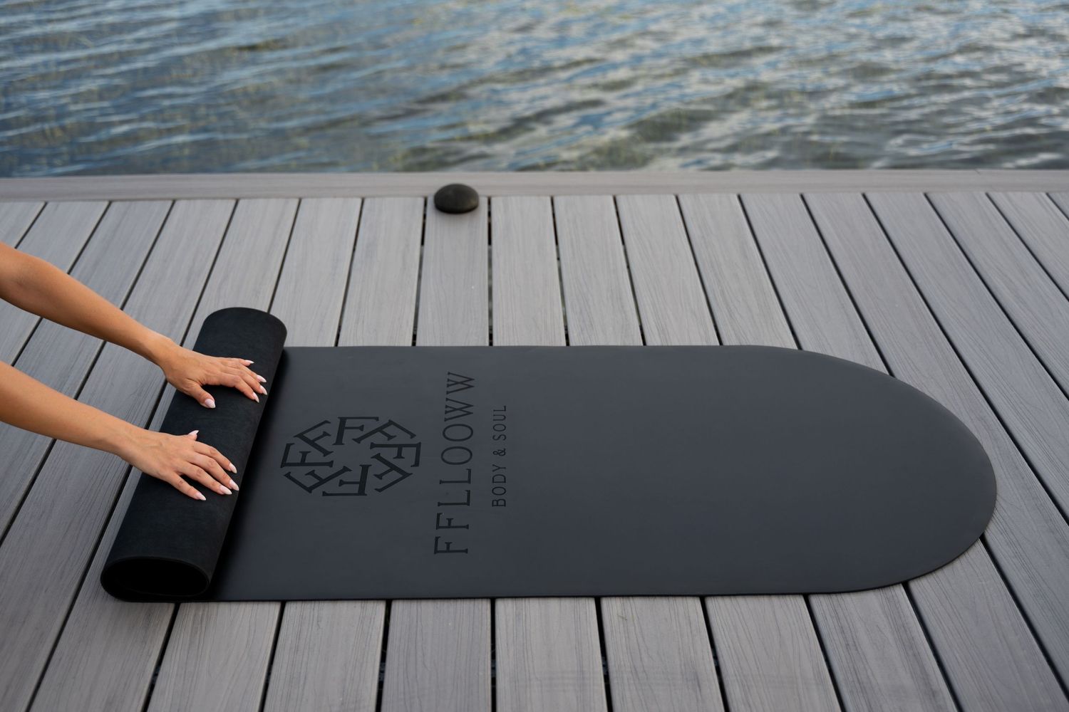 Black exercise mat displayed on wooden deck with water view.
