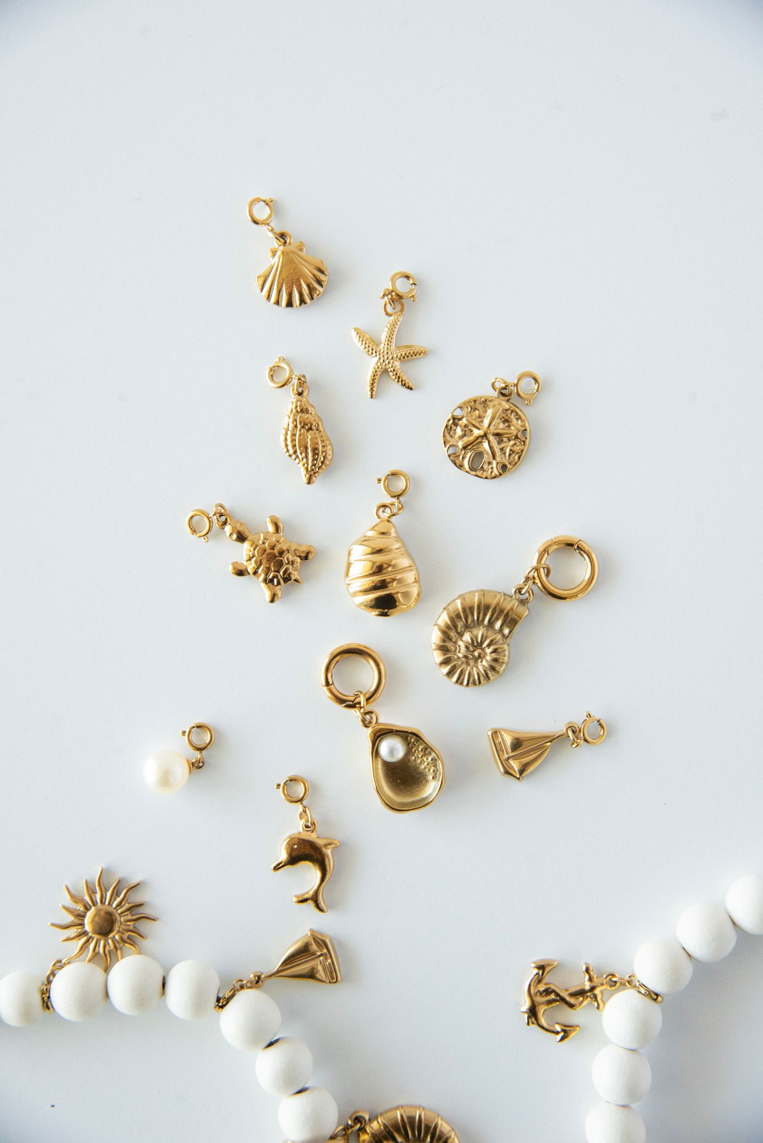 Gold plated jewelry charms and white beads scattered on white surface.