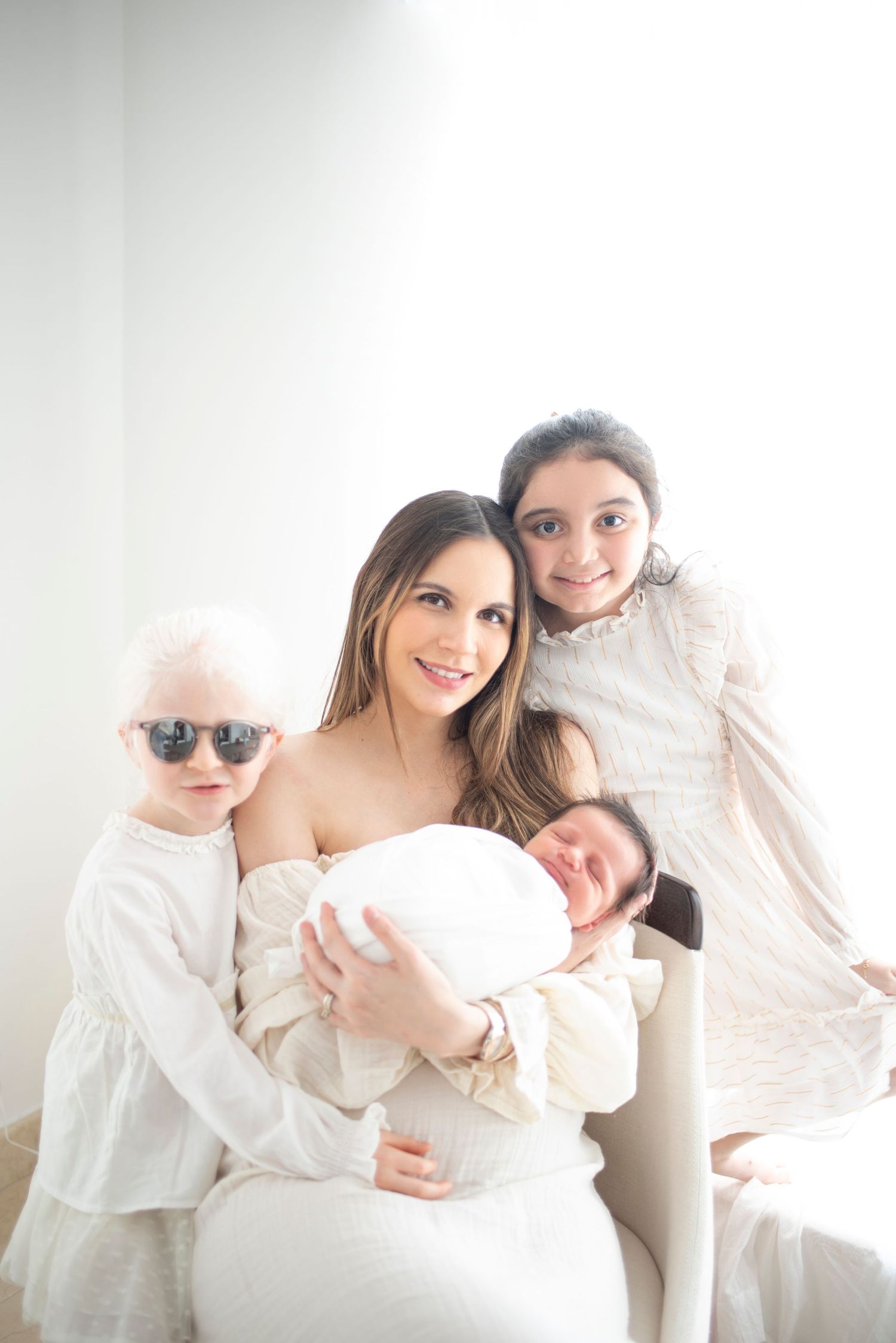 Family in white outfits poses together against bright white background.