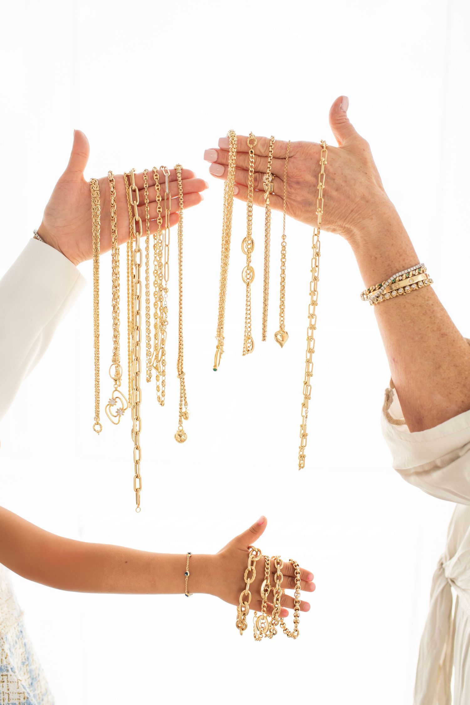 Hands holding multiple gold chain necklaces against white background.